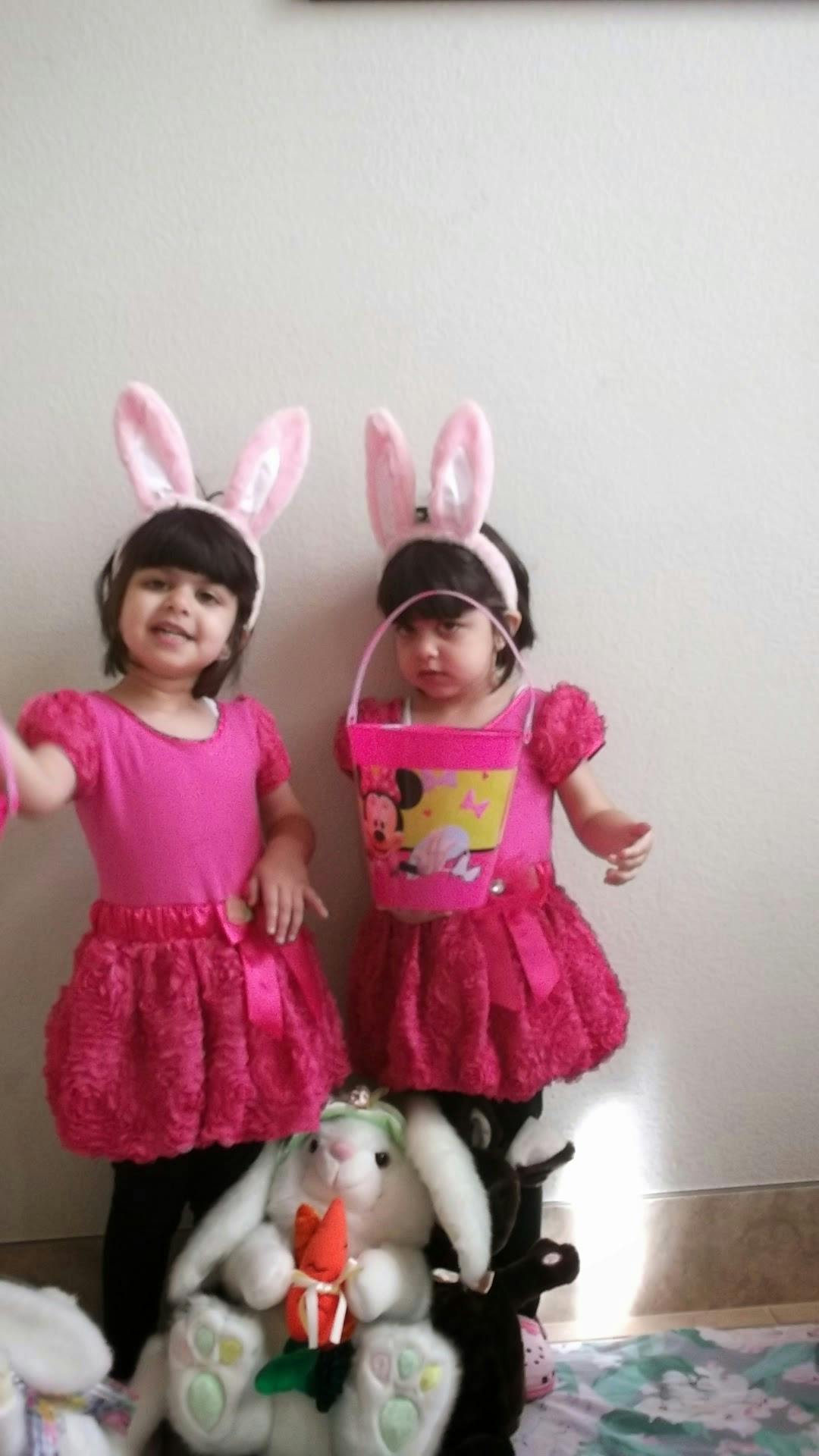 Two children wearing pink bunny ears and dresses, one holding a pink bucket