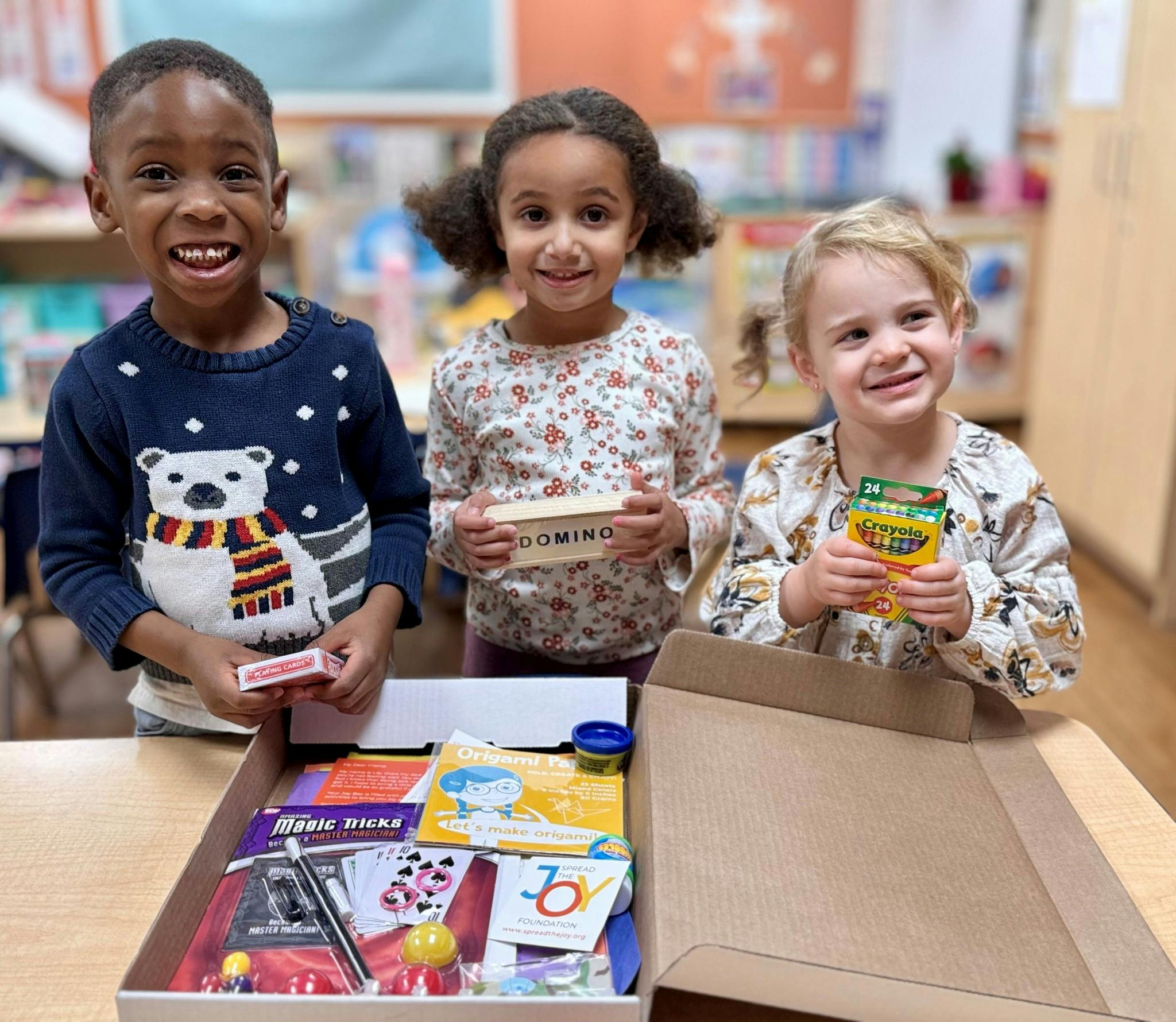Three children standing around an open box of games and activities