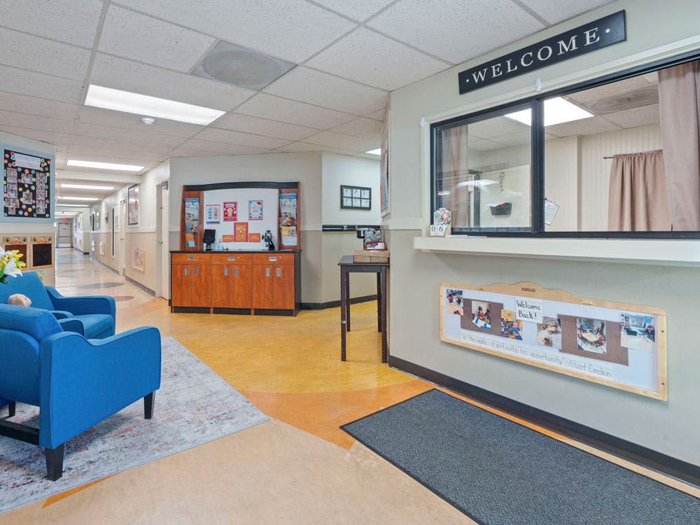 Lobby area with blue chairs, service window with Welcome sign, and bulletin board