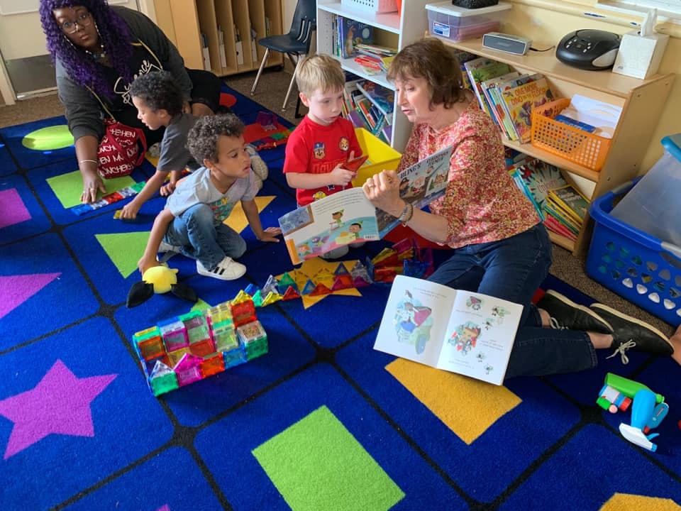 Adults and children reading books and playing with toys in a classroom