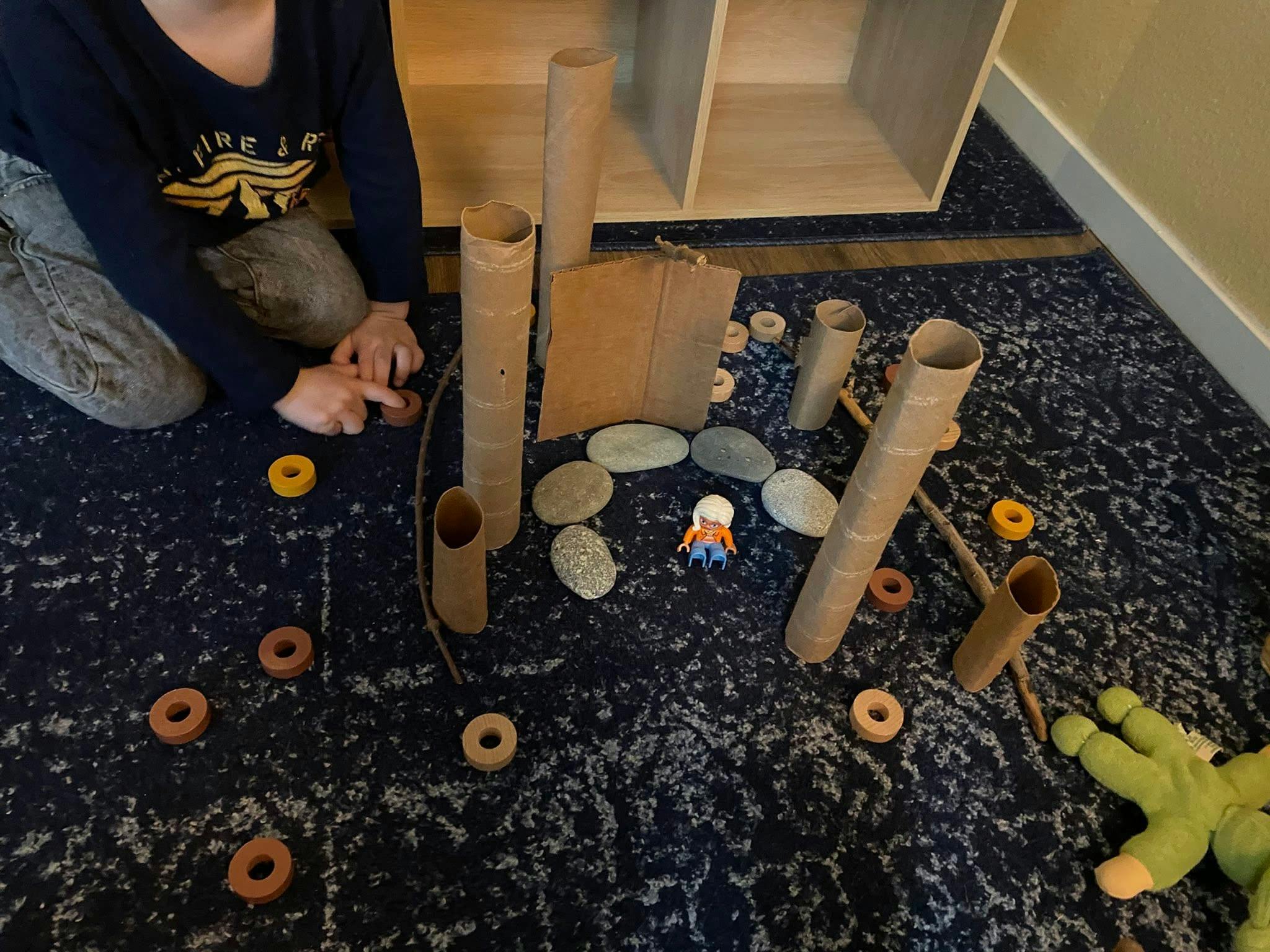 Child playing with cardboard tubes, rocks, and wooden rings on a carpet
