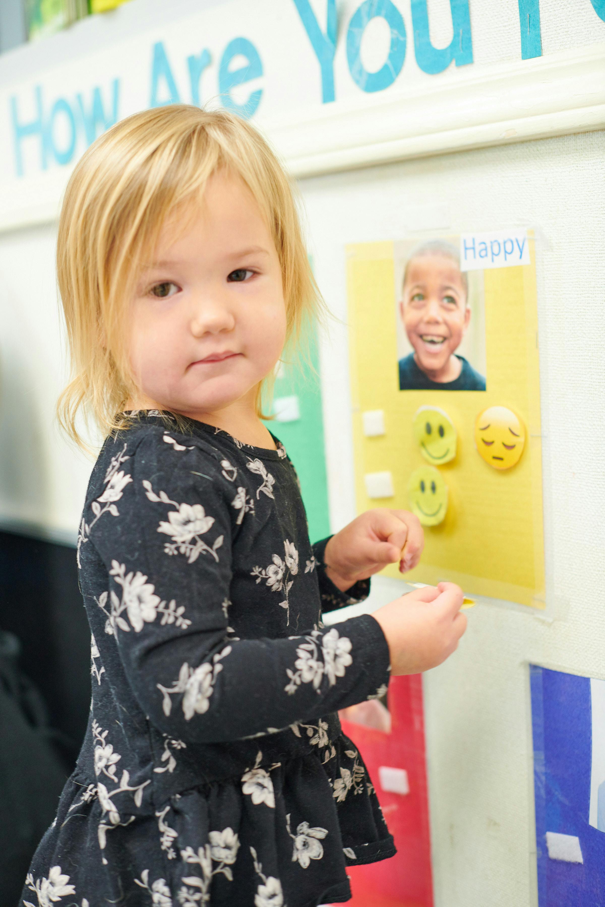 Child standing next to a wall display with a picture and emoji faces