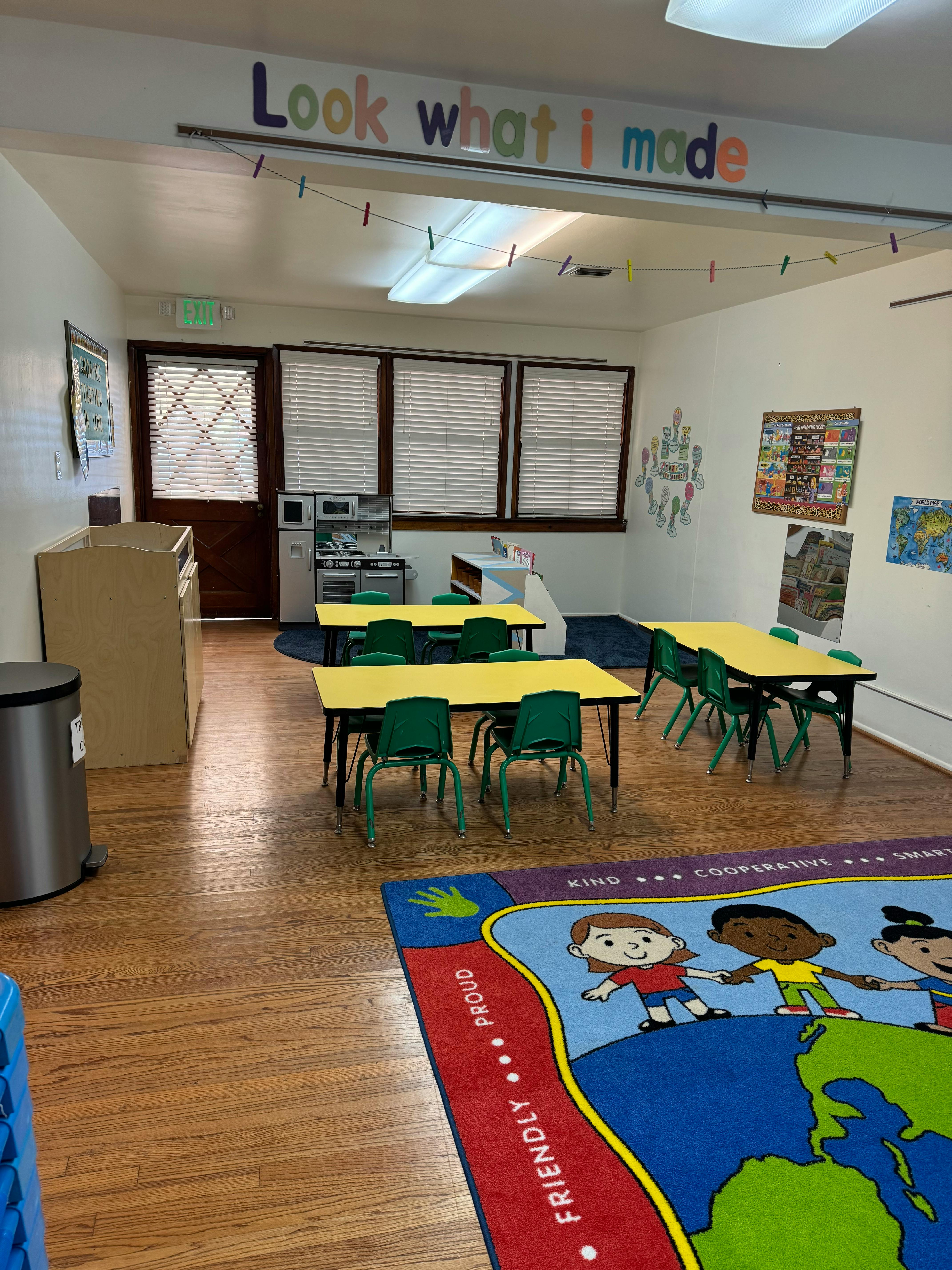 Classroom with small tables and chairs, and a rug with children on a globe