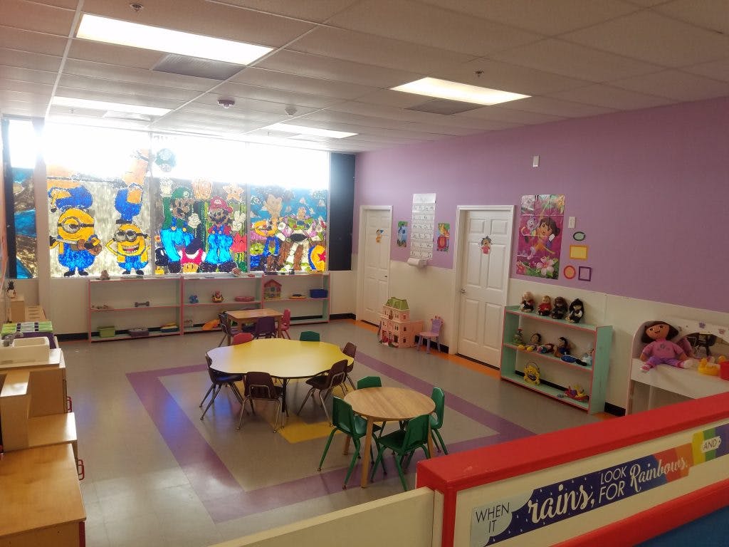 Empty classroom with small tables and chairs, decorated with cartoon characters