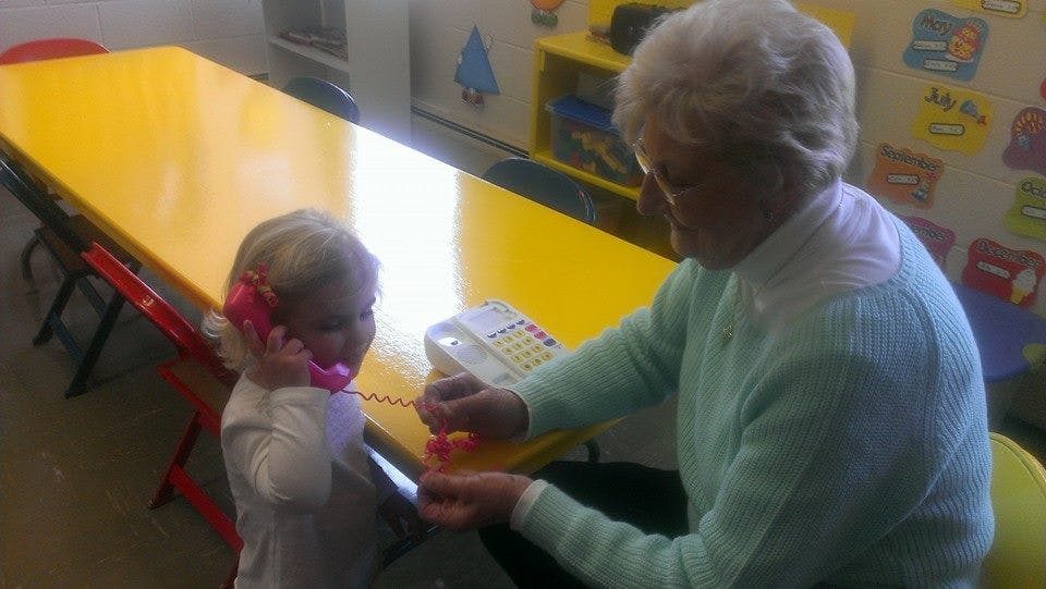 Child holding a pink toy phone to ear with an adult nearby