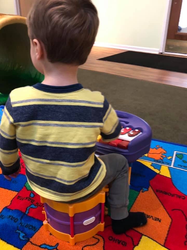 Child sitting on a toy drum playing with a toy piano