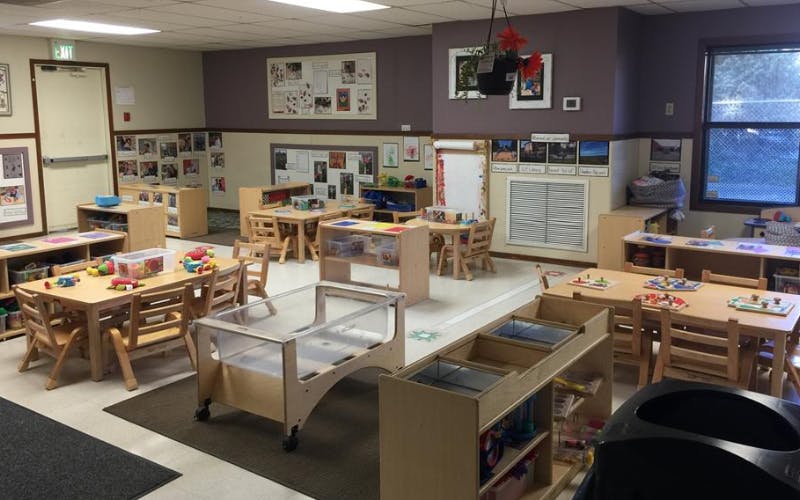 Classroom with multiple wooden tables and chairs, toys, and learning materials