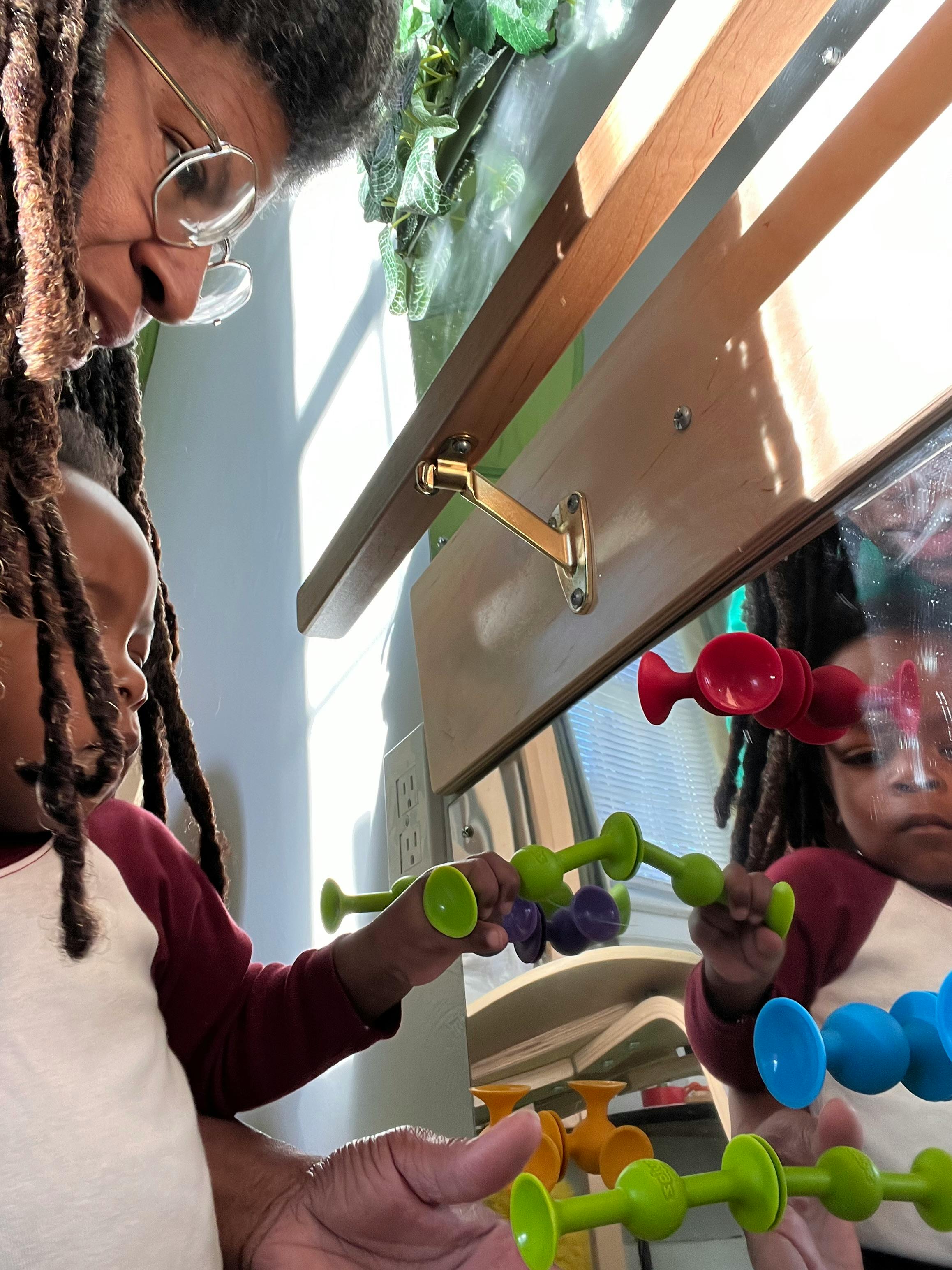 Person and child playing with colorful suction cup toys on a mirror