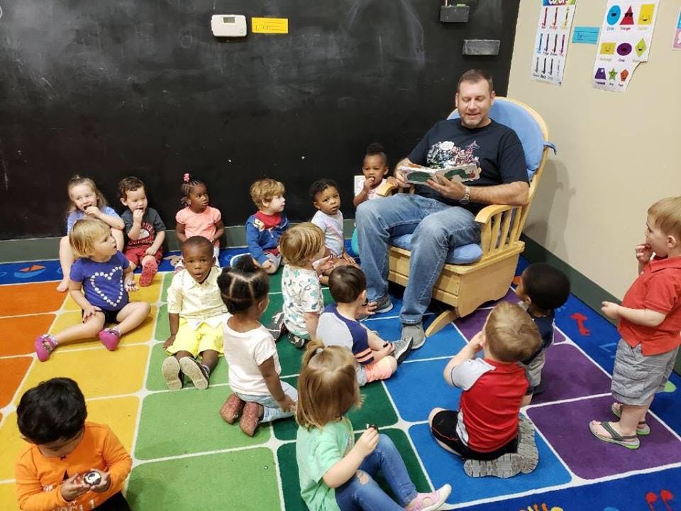 Person reading a book to a group of children in a classroom