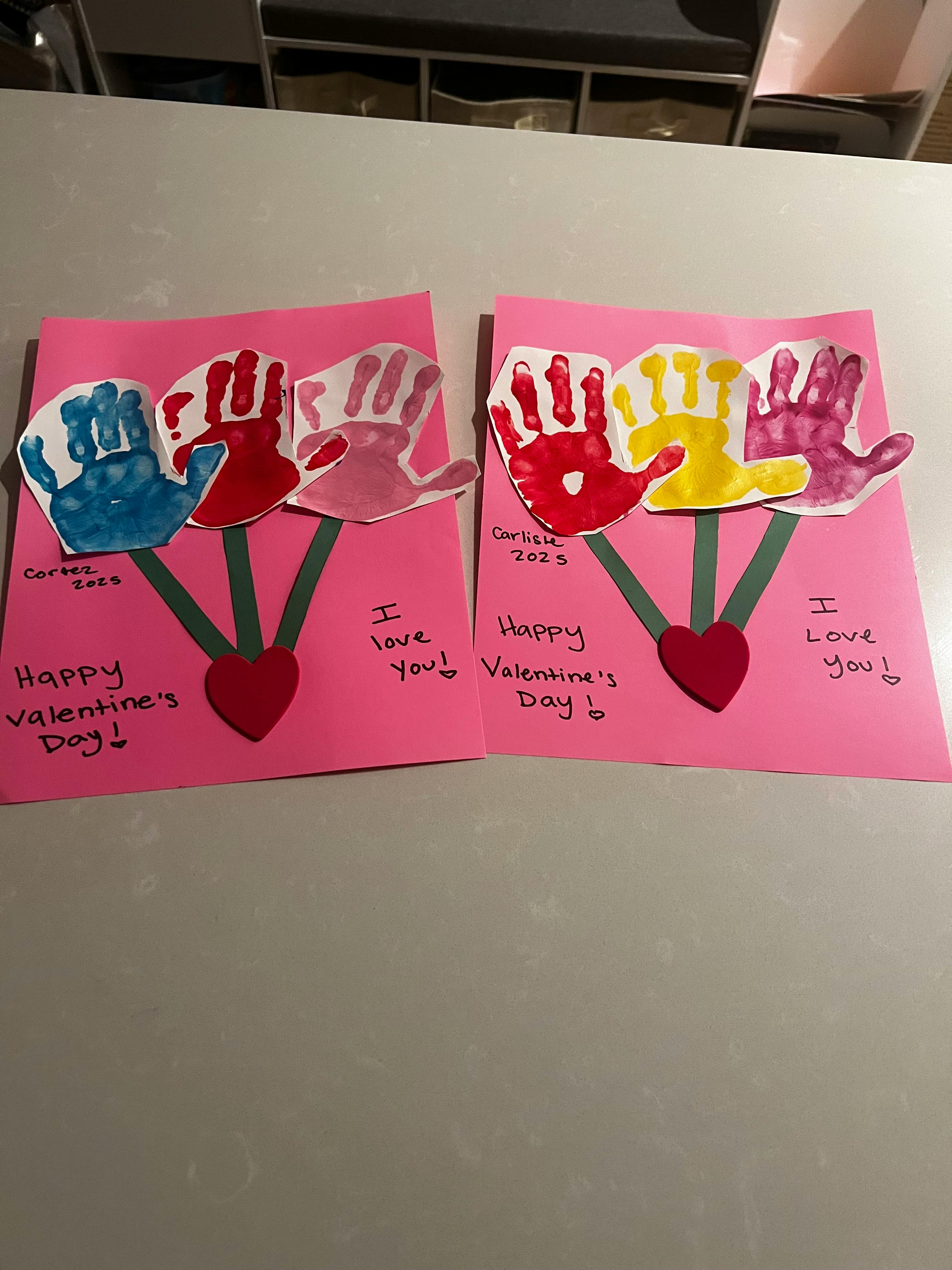 Two pink cards with colorful handprints and "Happy Valentine's Day" written on them