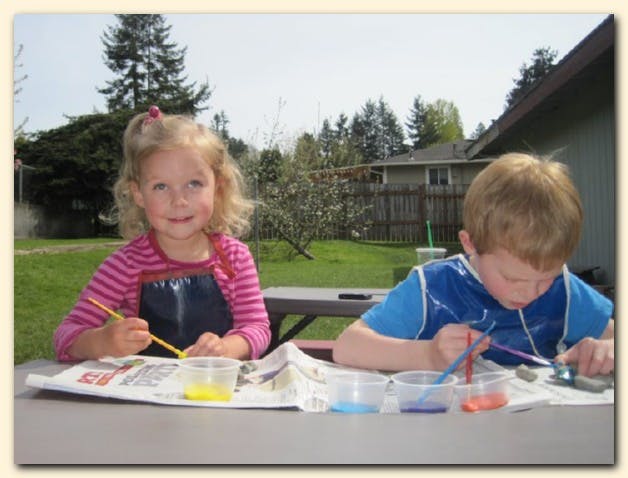 Two children painting outdoors at a table
