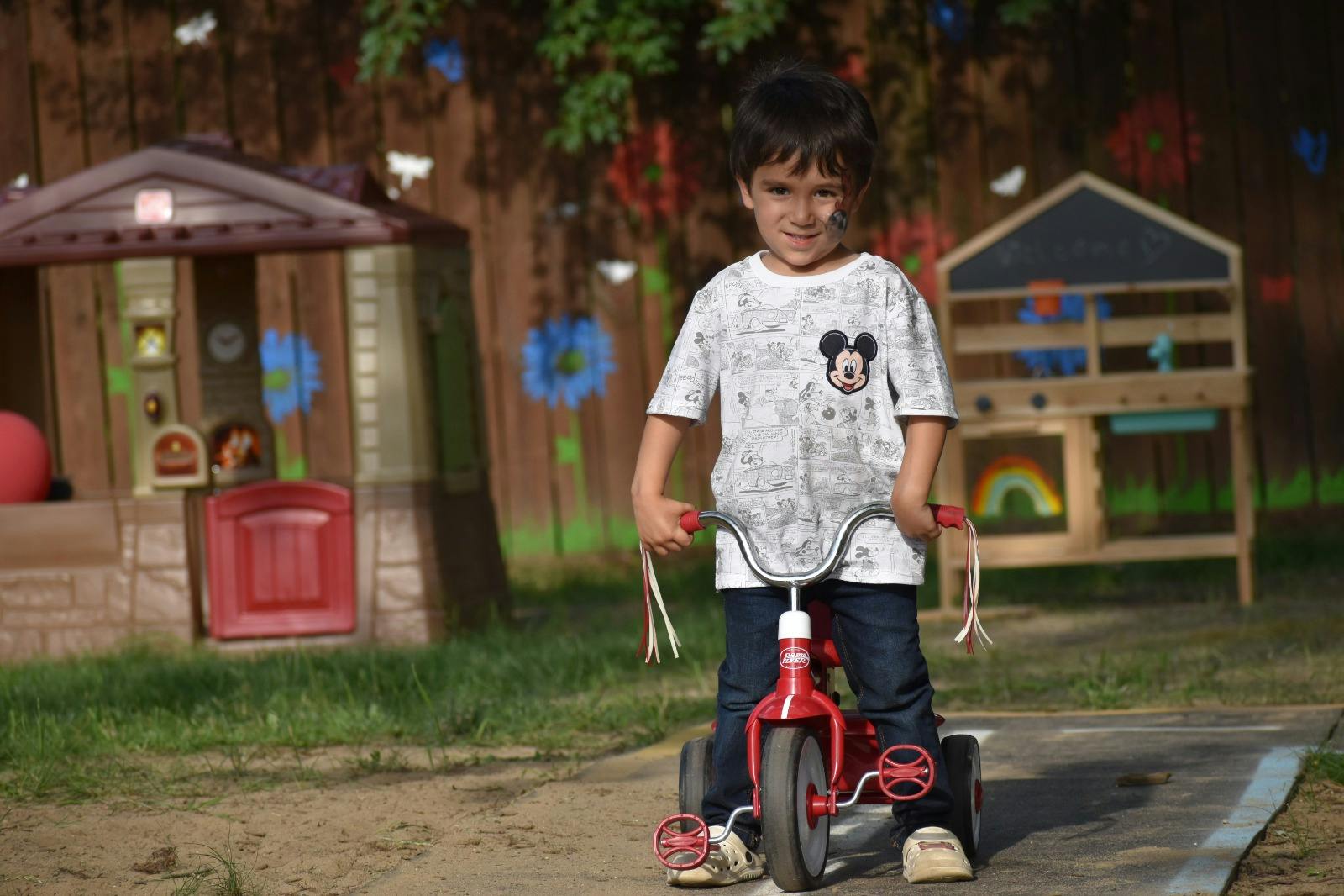 Child sitting on a red tricycle in an outdoor play area