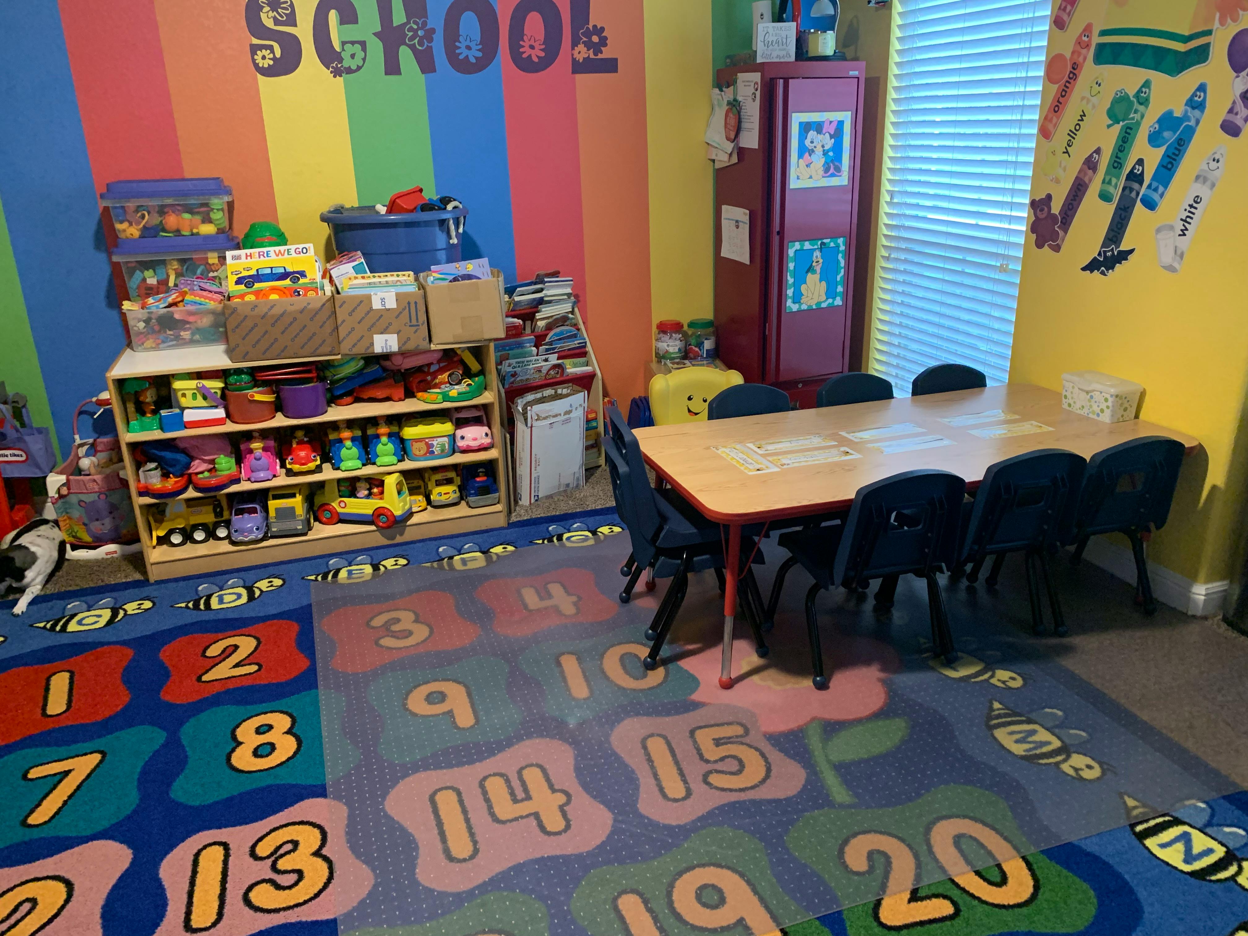 Classroom with a table and chairs, toy shelves, and a number rug