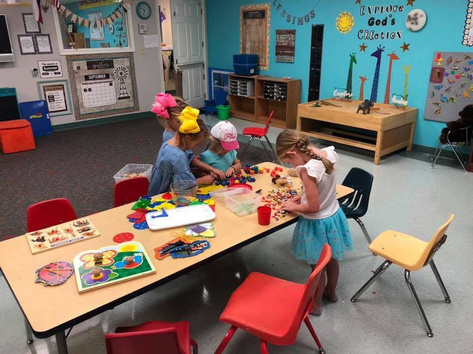 Children playing with blocks and toys at a table in a classroom