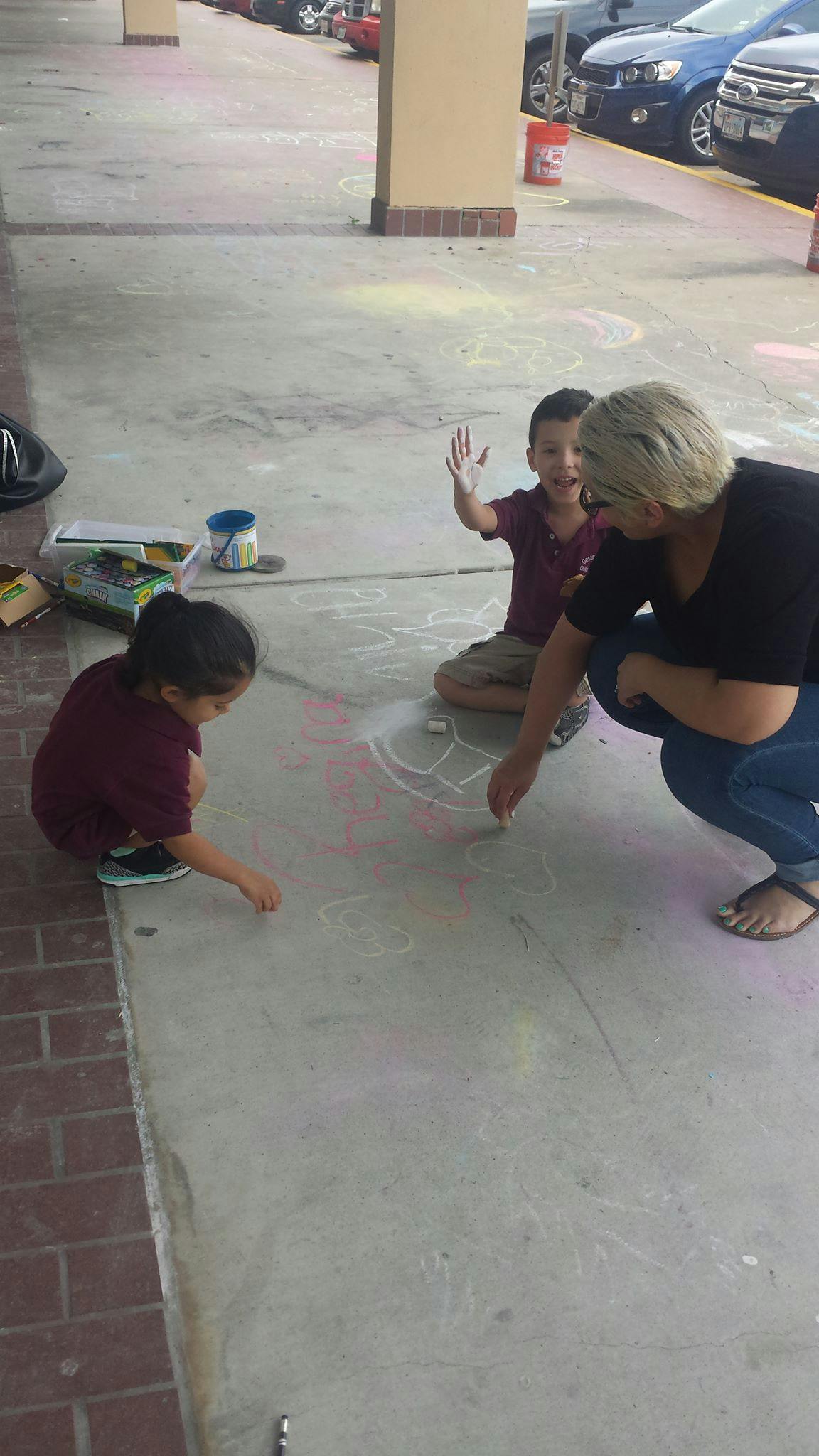 Adult and two children drawing with chalk on a sidewalk