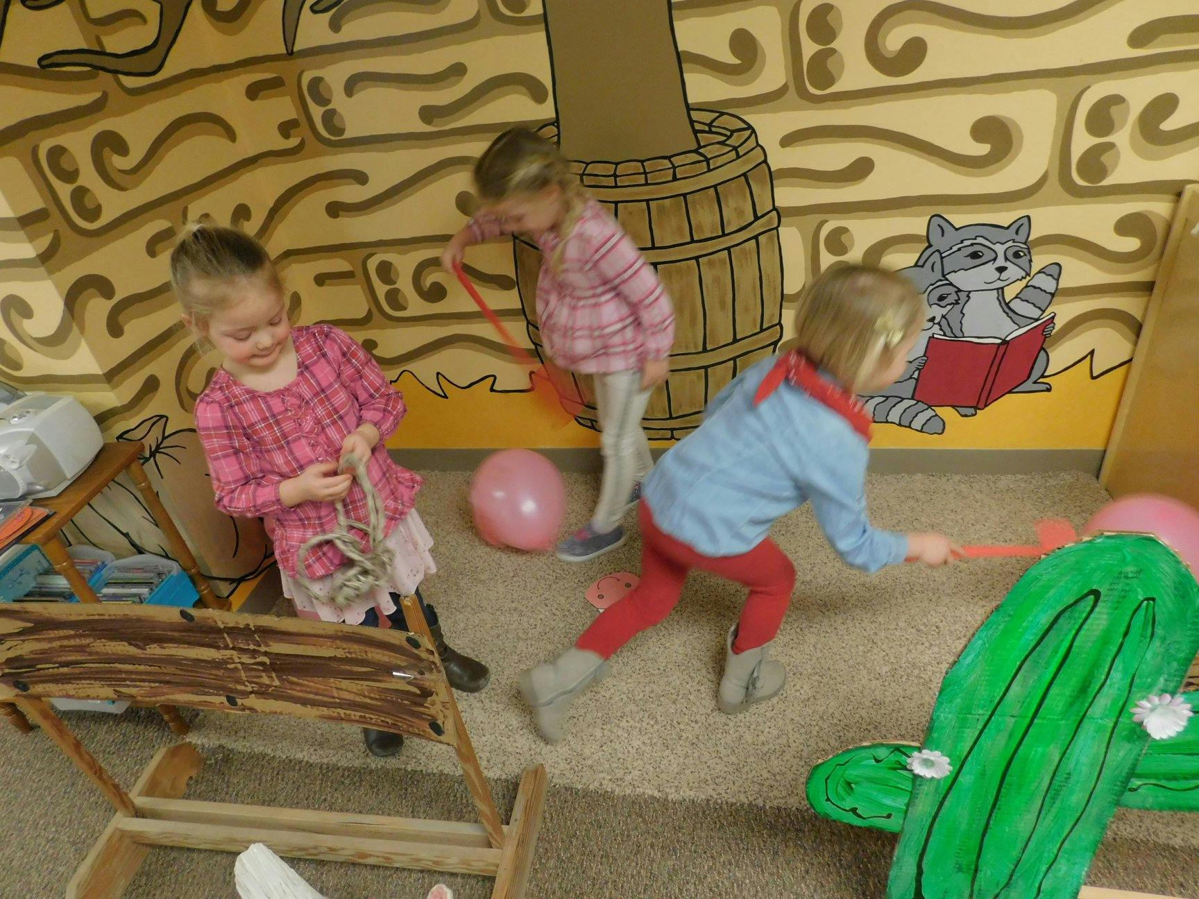 Three children playing with toys and a pink balloon