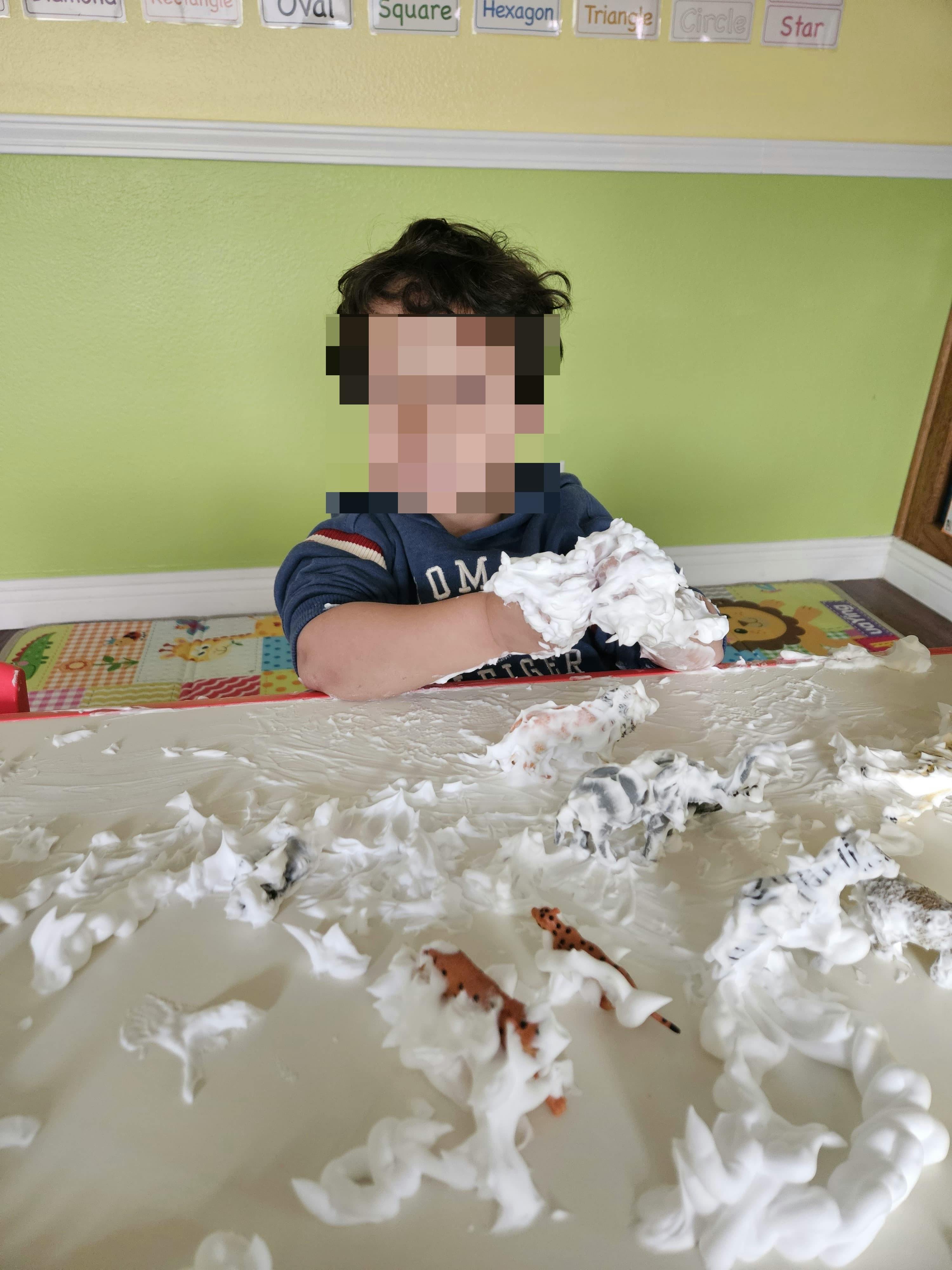 Child playing with shaving cream and toy animals