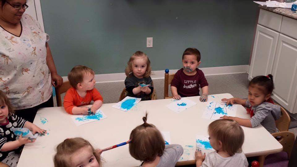 Adult and multiple children sitting at a table with blue paint