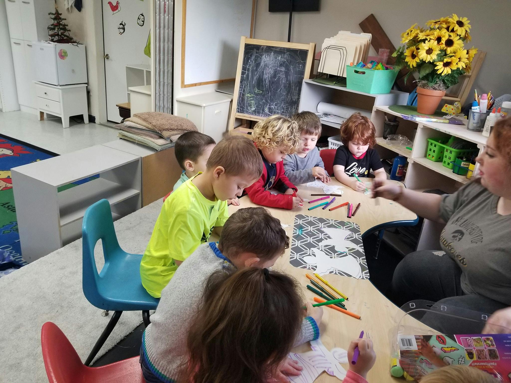 Adult and children coloring at a table in a classroom