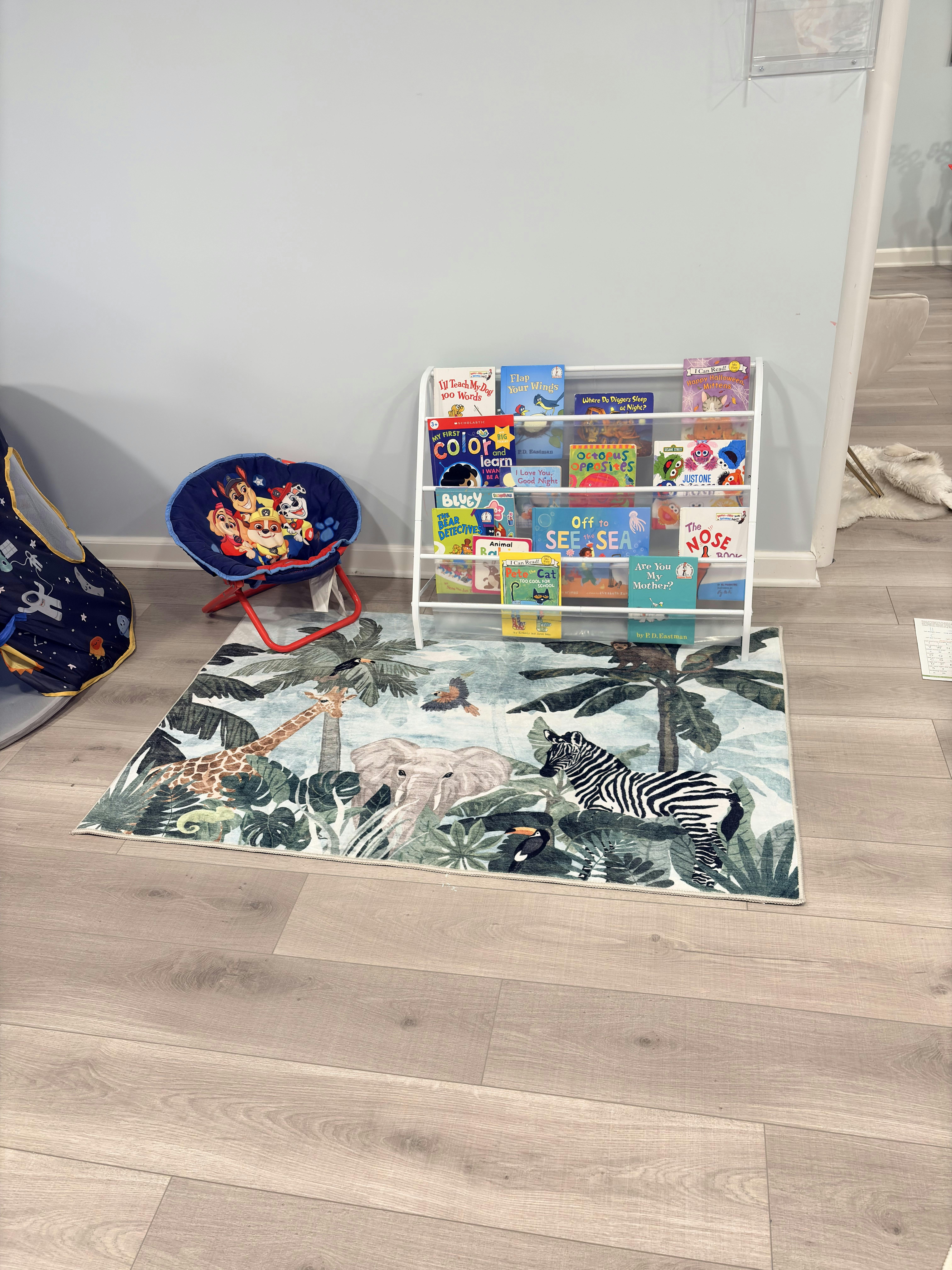 A children's reading nook with a bookshelf, a blue chair, and a jungle-themed rug