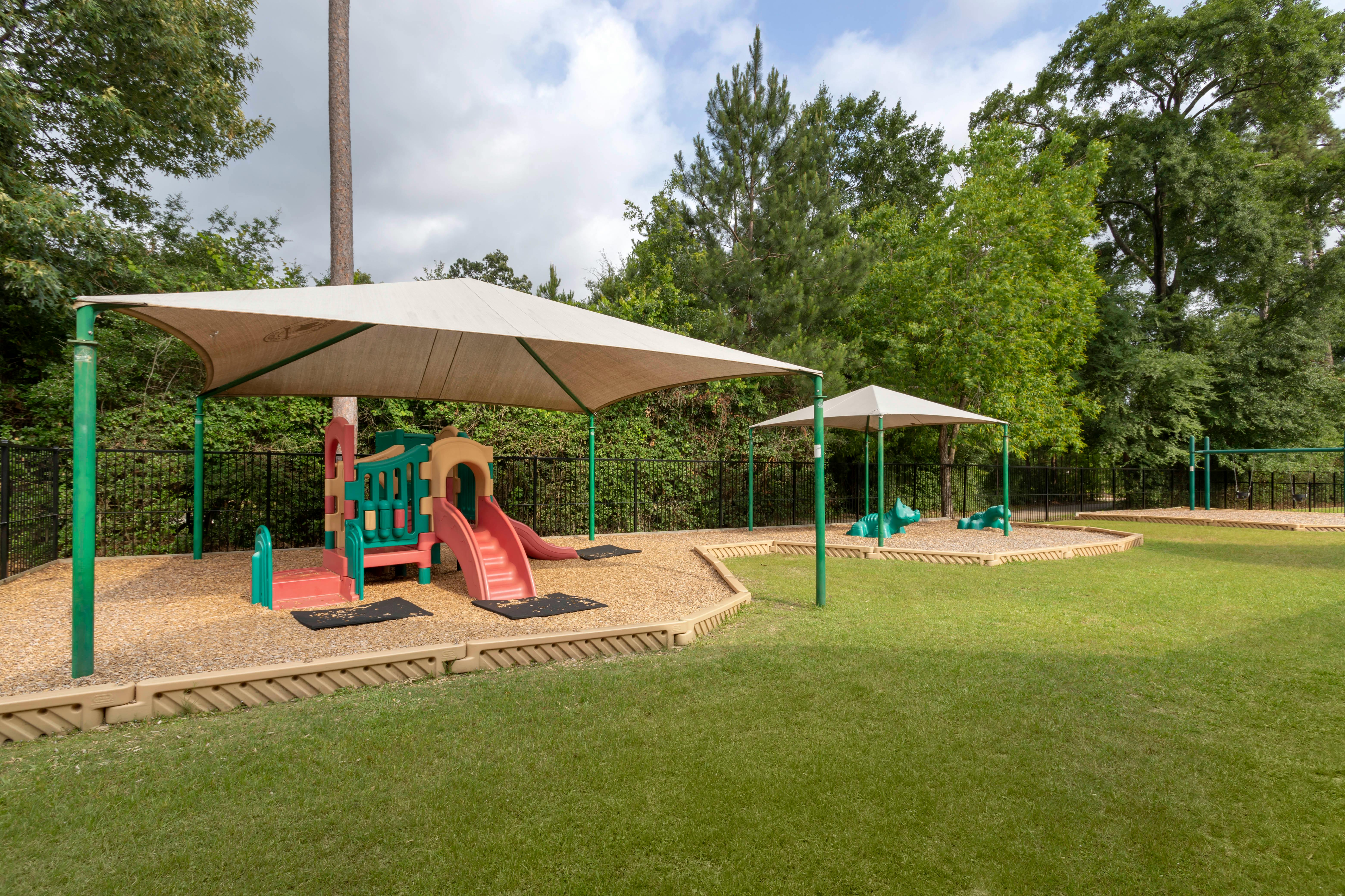 A colorful playground with slides and animal spring riders, under shade canopies