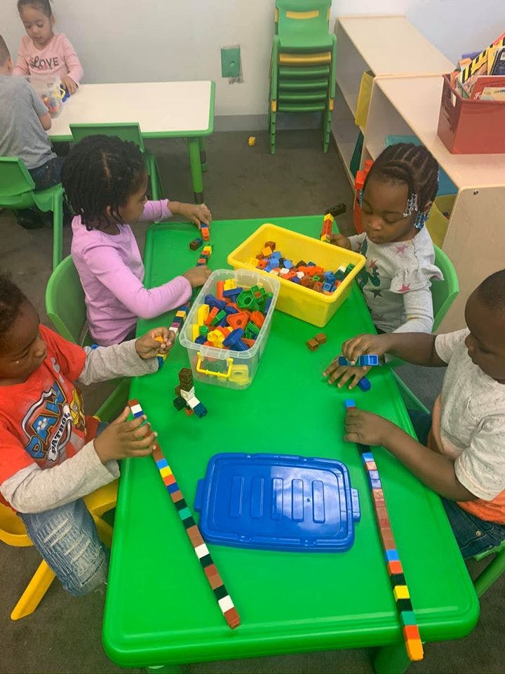Four children playing with colorful building blocks at a green table