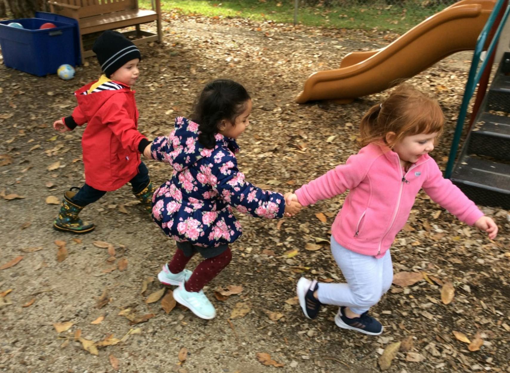Three children holding hands and running outdoors