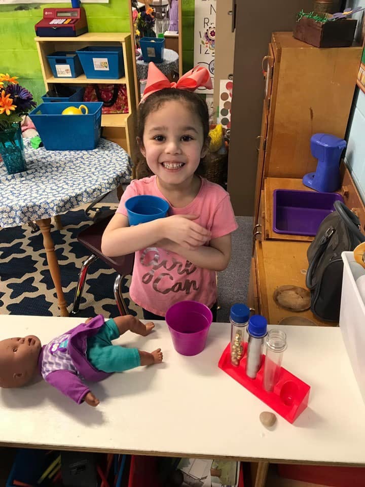 Child holding a blue cup and smiling in a classroom