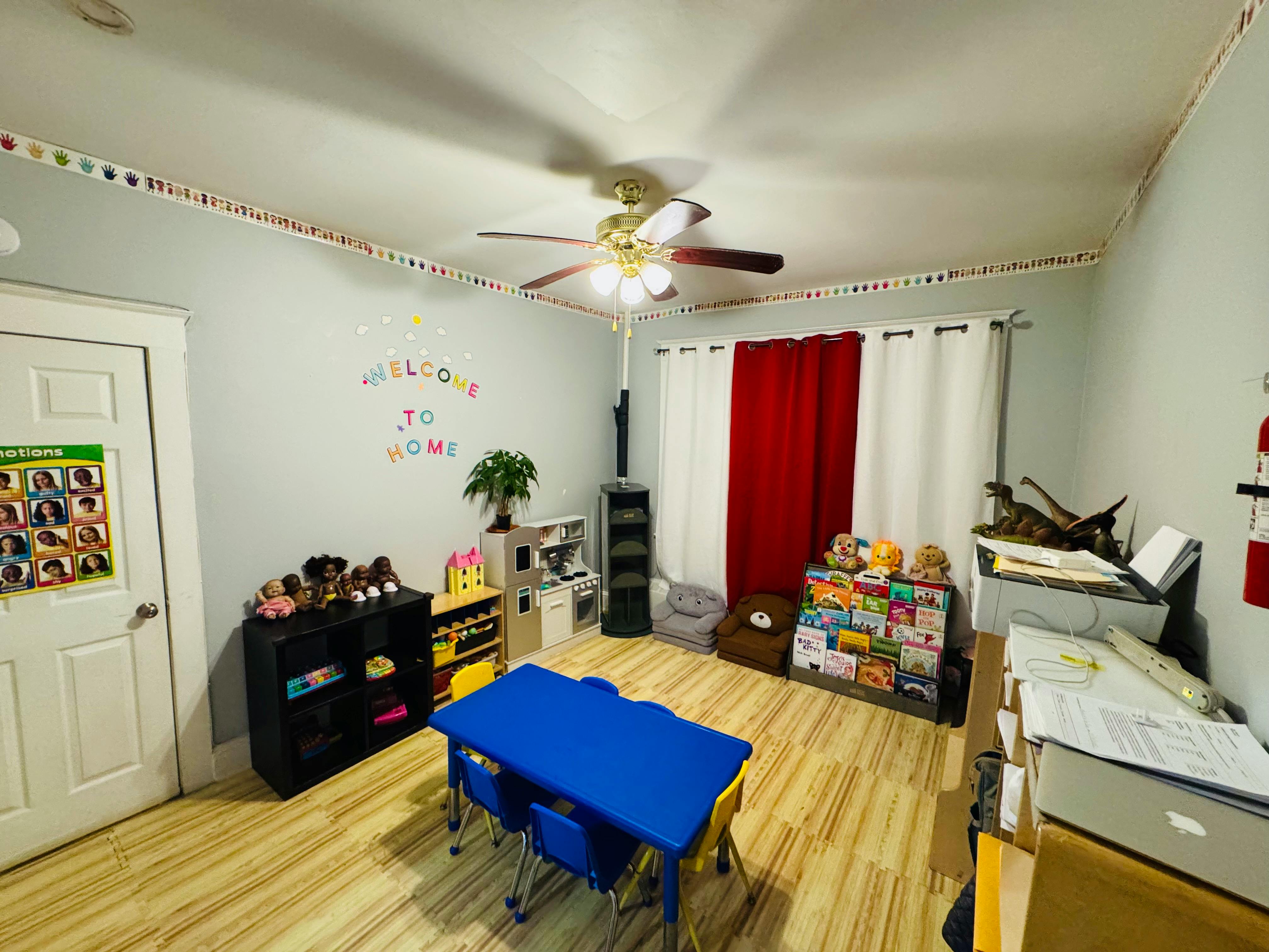 Classroom with a blue table and chairs, shelves, and red and white curtains
