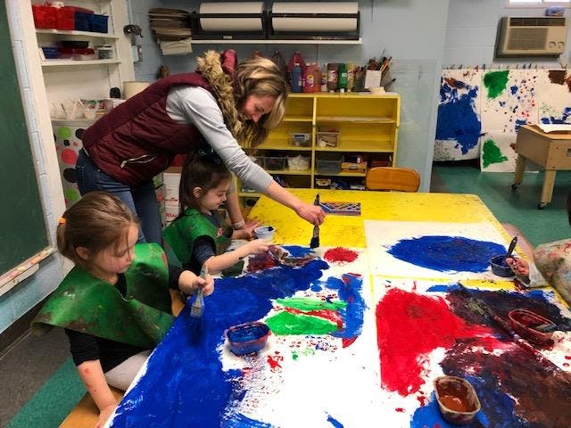 Adult and two children painting on a large sheet of paper
