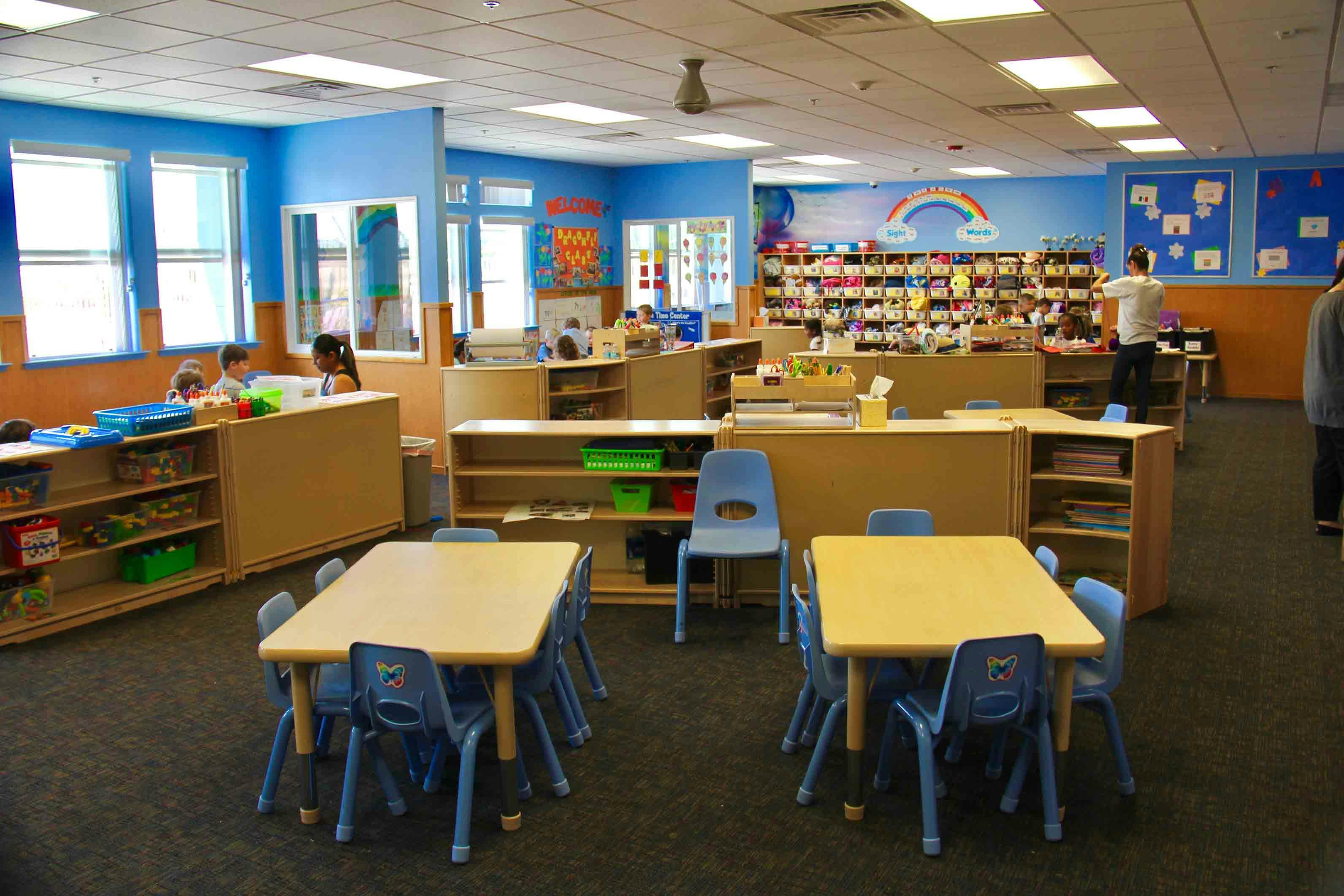 Classroom with small tables and chairs, shelves, and a rainbow mural