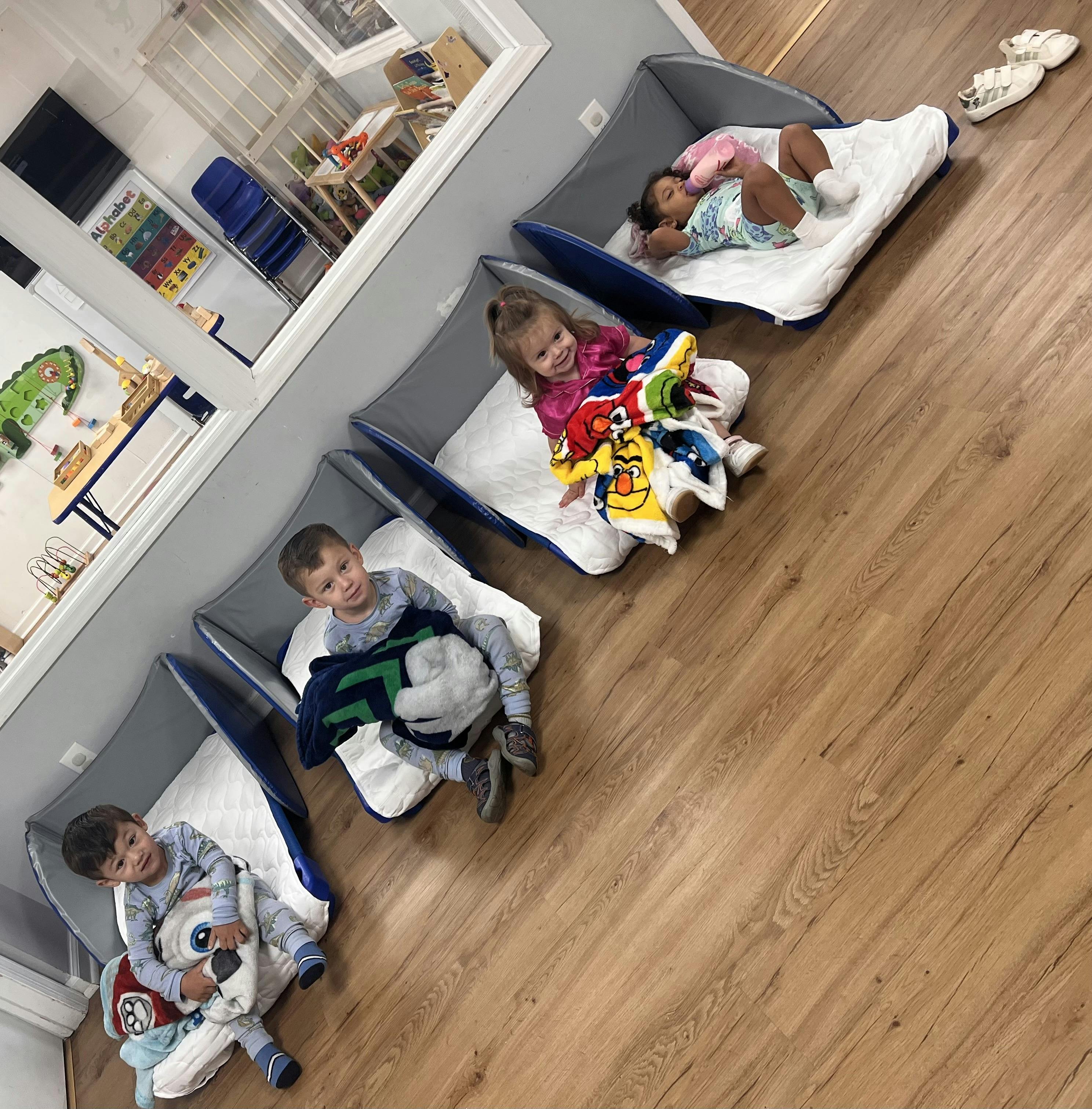 Four children resting in cots in a classroom