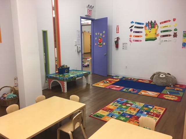 Classroom with small tables and chairs, colorful rugs, and a purple door