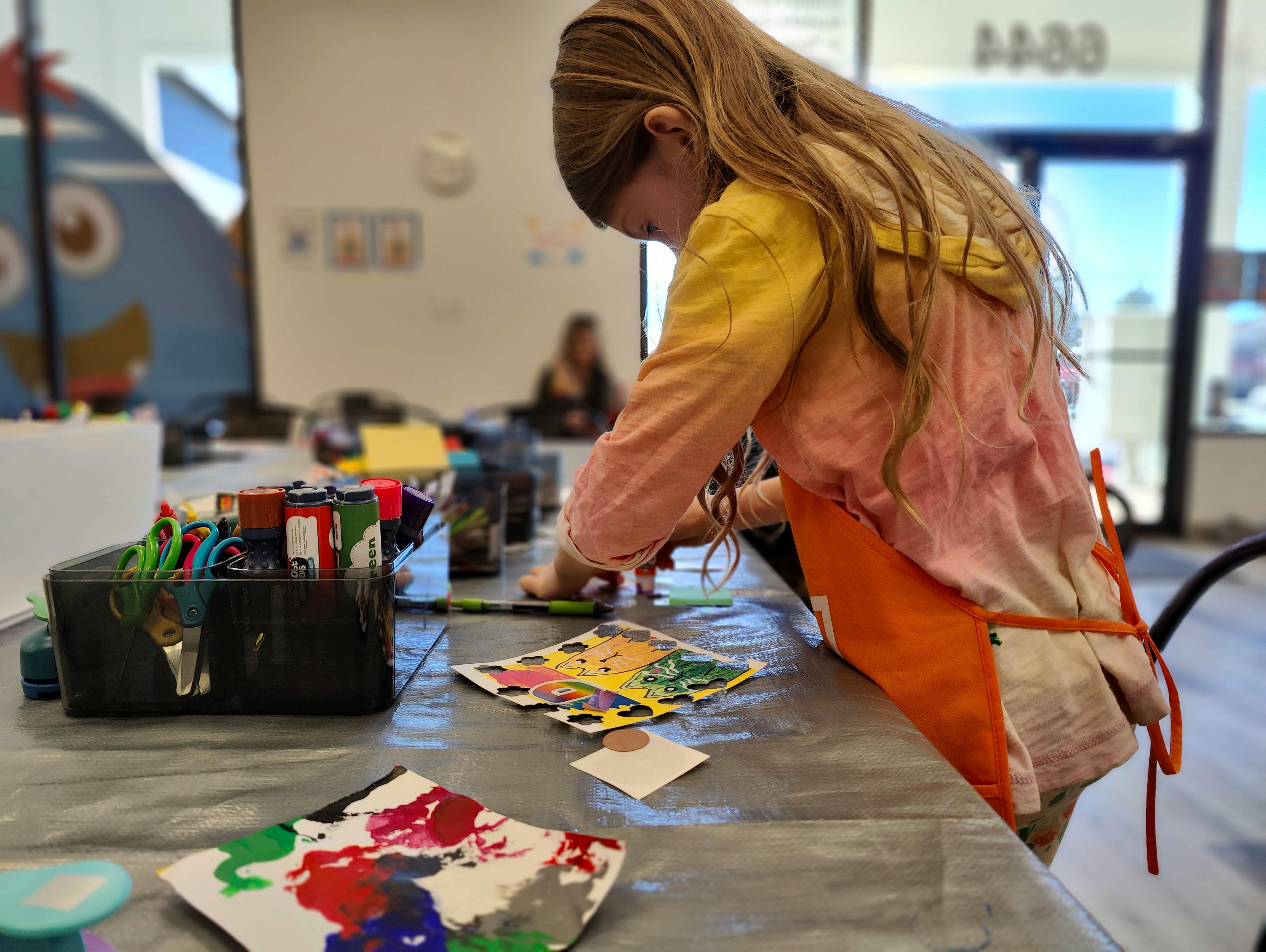 Child wearing an orange apron and drawing on paper