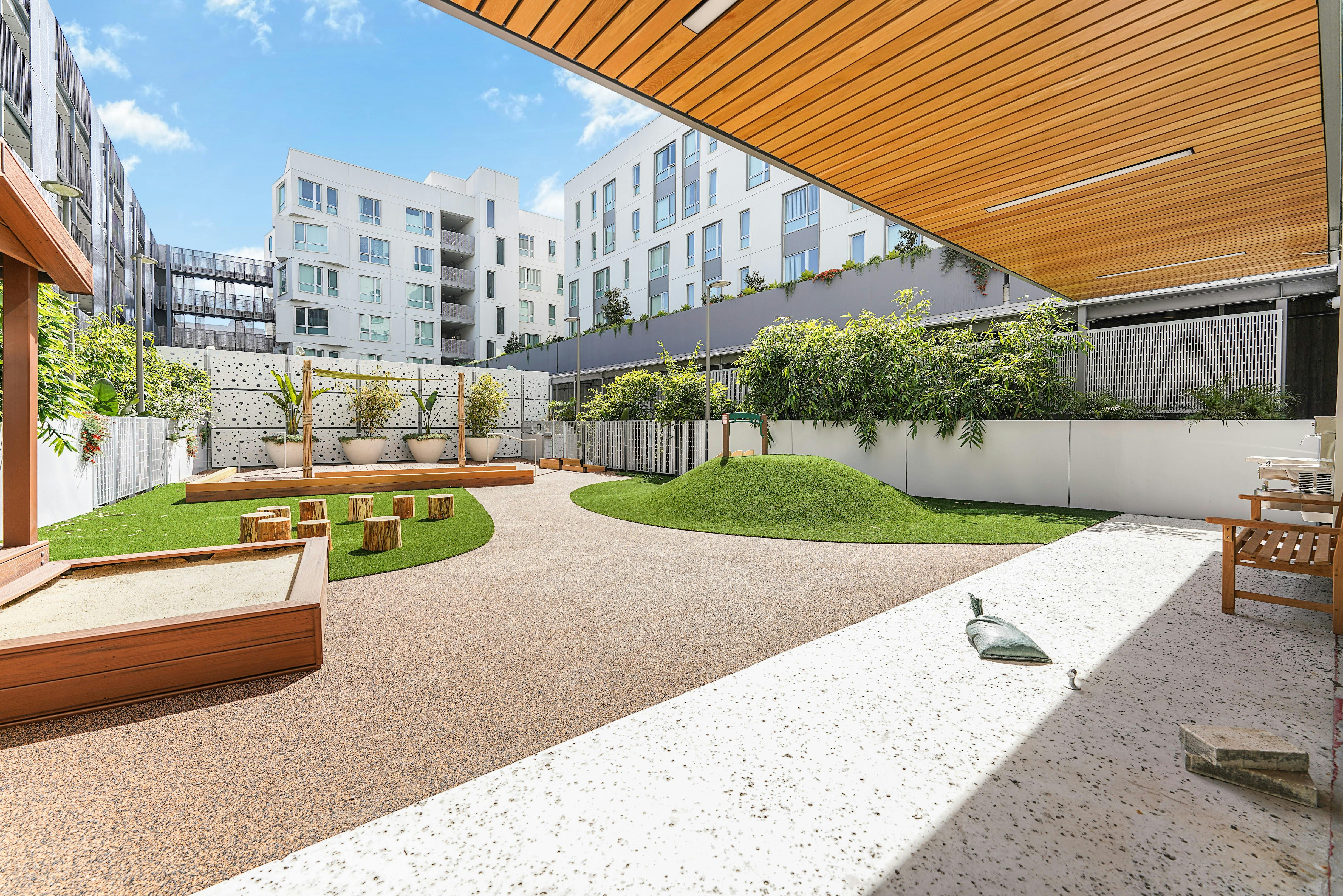 Outdoor playground area with sandbox, grassy hill, and wooden seating