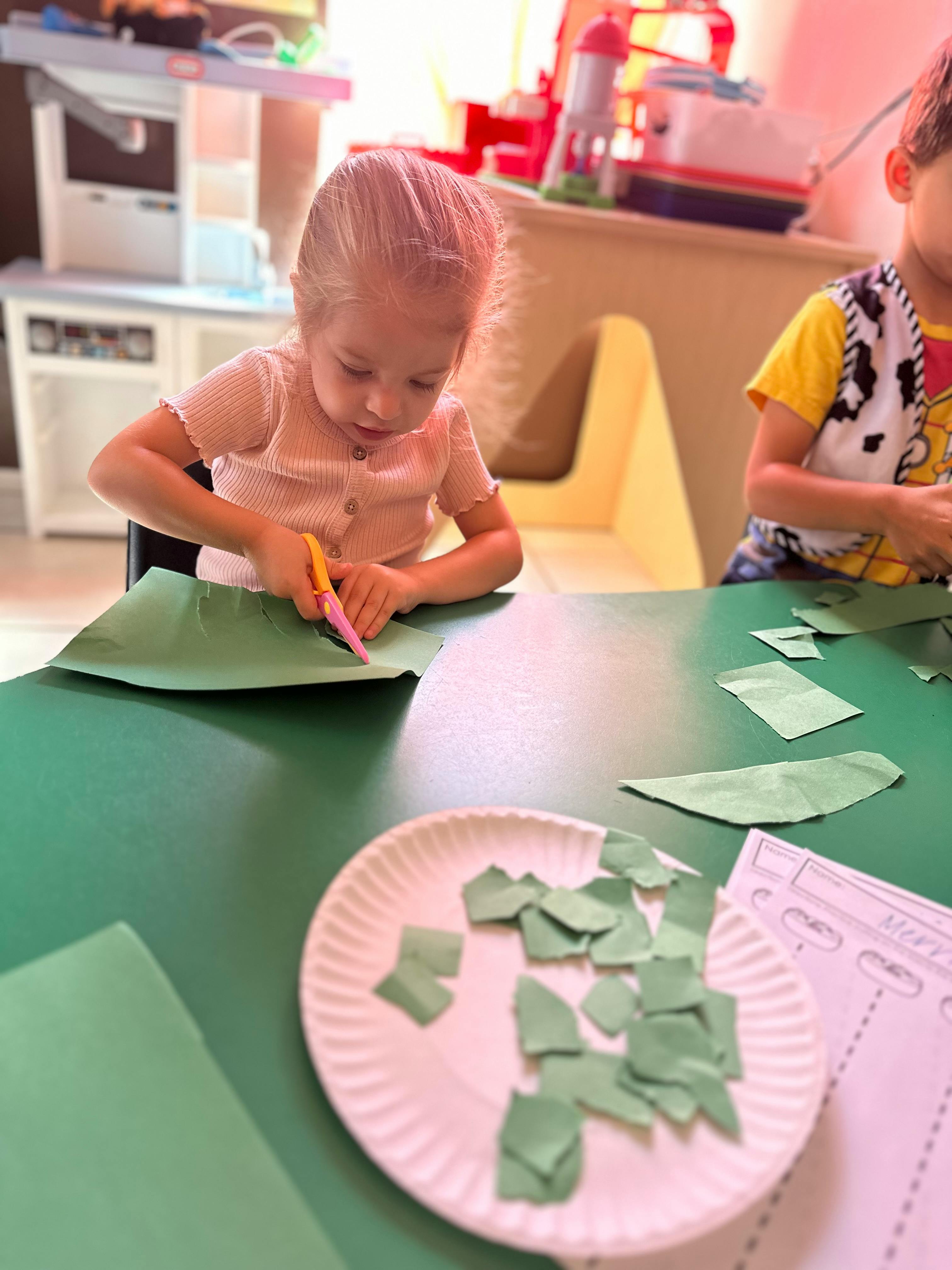 Child cutting green paper with scissors at a table