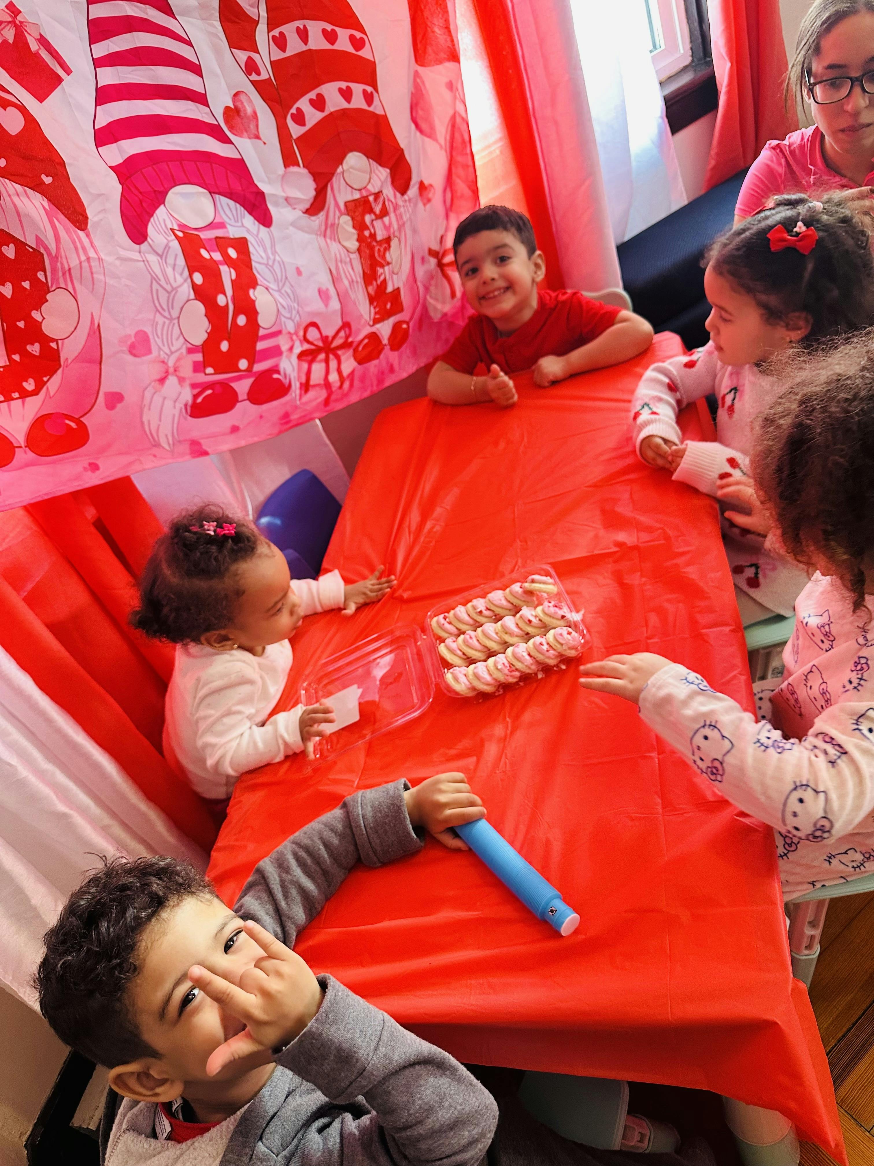 Group of children sitting at a red table with a container of cookies