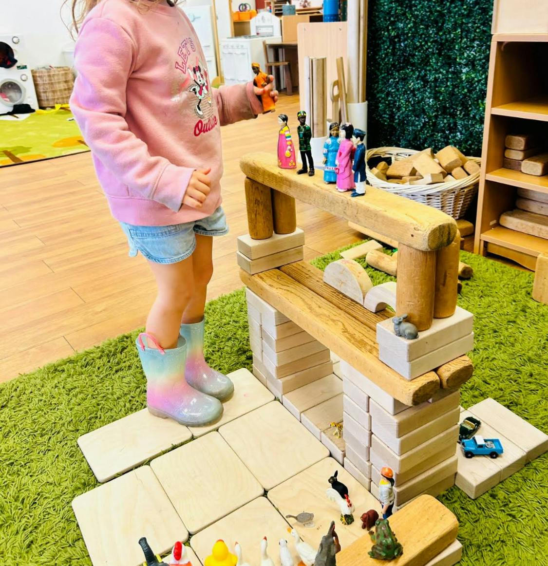 Child standing on wood blocks next to toy figures on a block structure