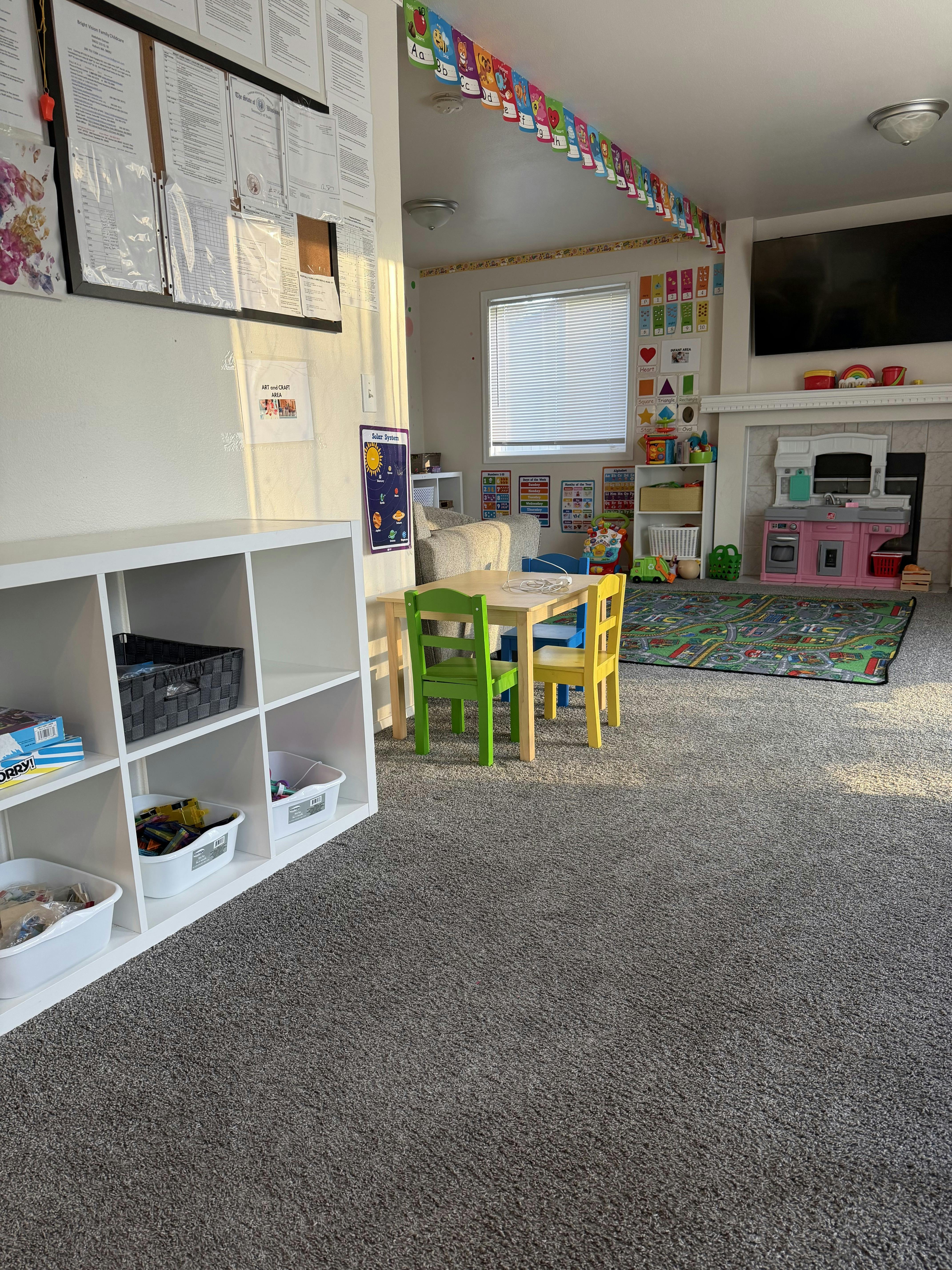 Childcare room with a small table, chairs, play kitchen, and educational posters