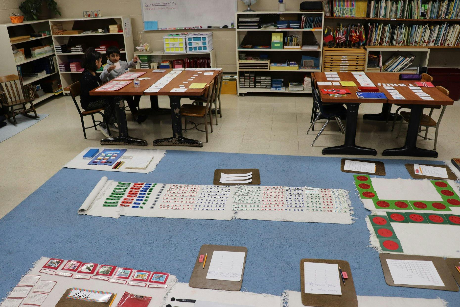 Classroom with tables, shelves, and learning materials on the floor