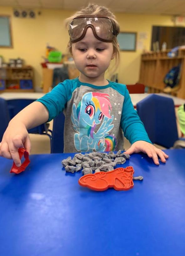 Child wearing goggles playing with modeling clay and cookie cutters