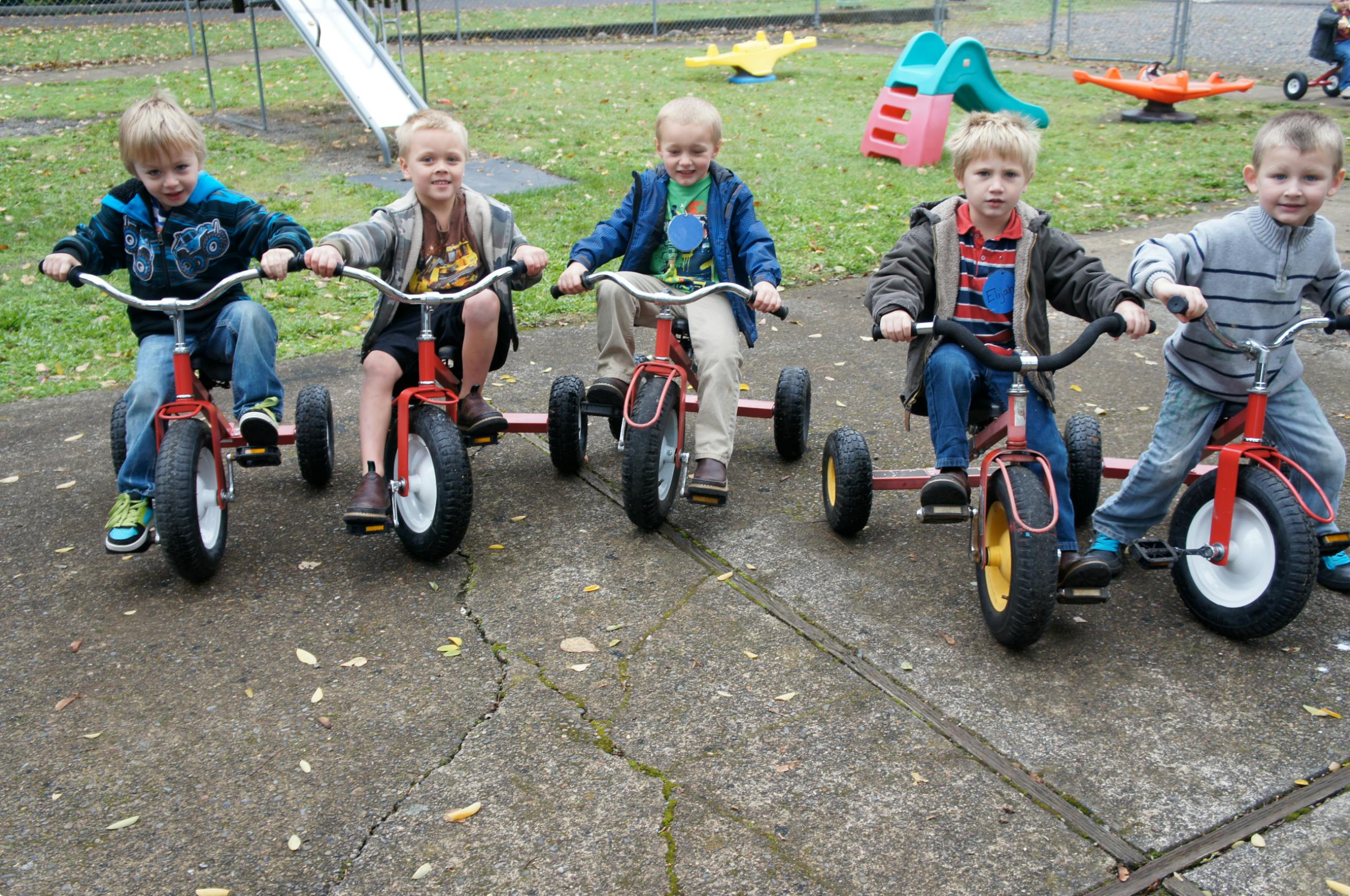 Five children riding tricycles outdoors