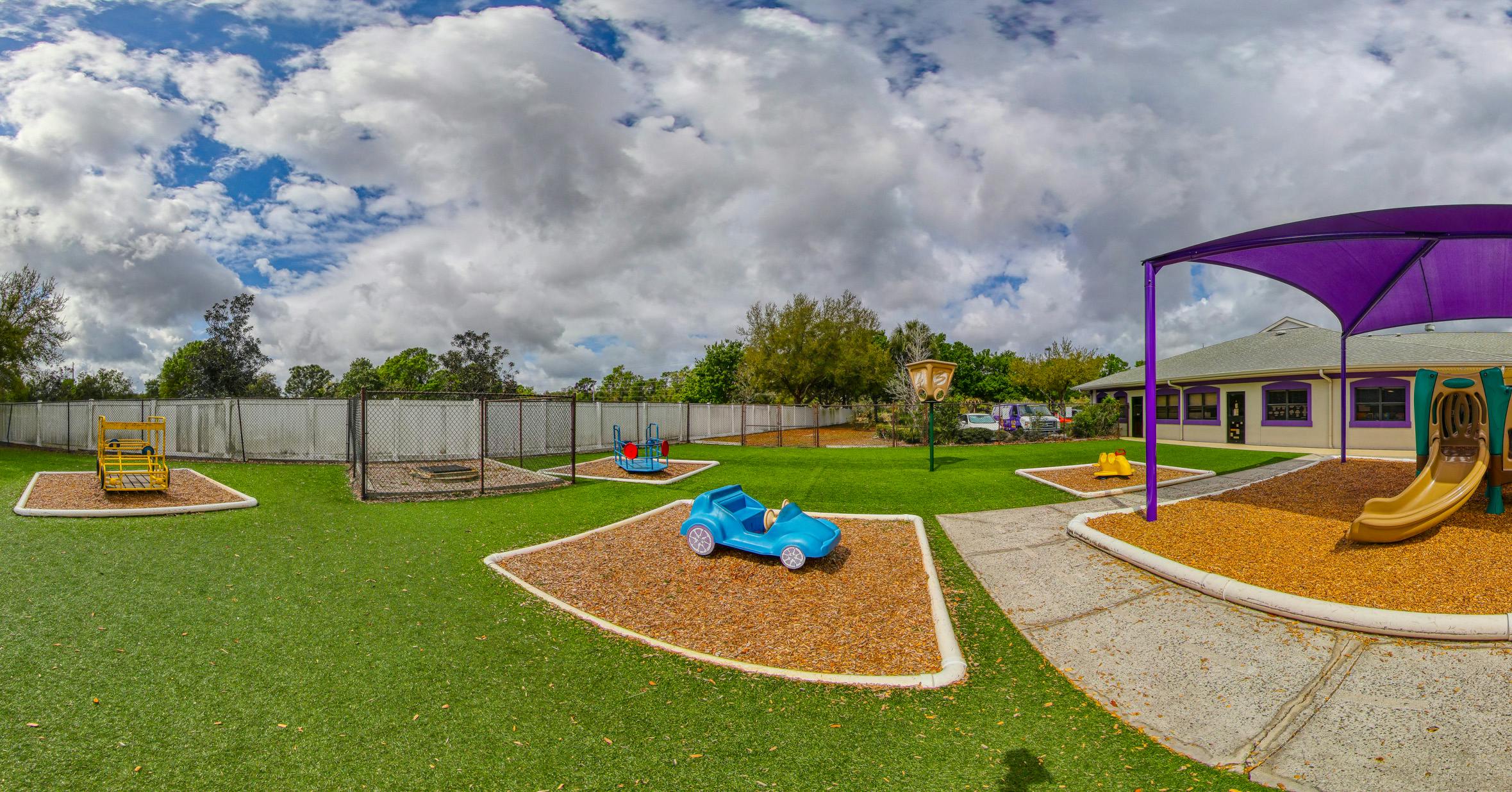 A childcare center playground with artificial grass, play structures, and a building