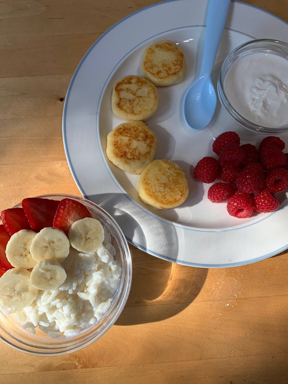 Pancakes, raspberries, and yogurt on a plate with a bowl of fruit and cottage cheese
