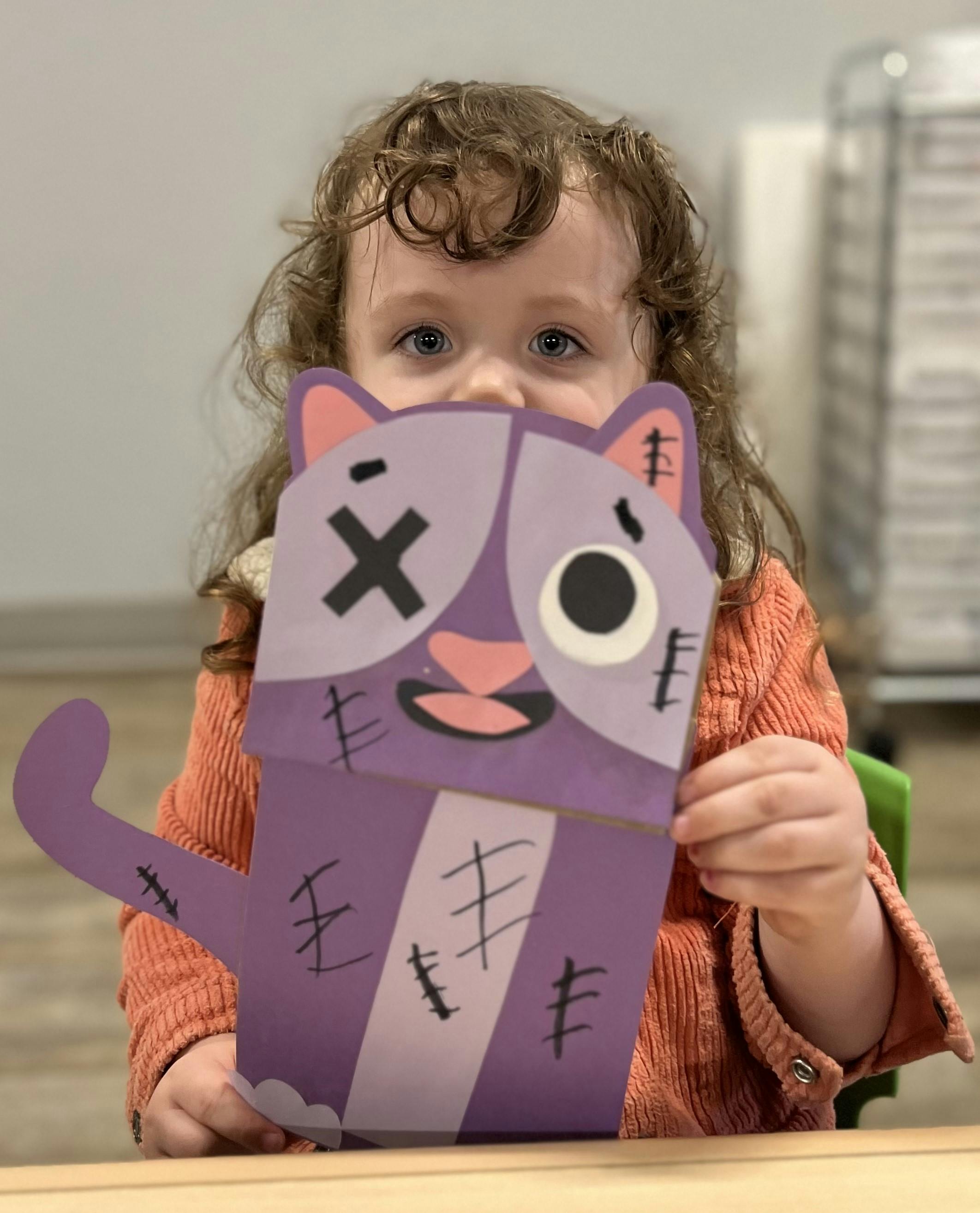 Child holding a purple paper cat craft