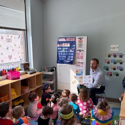 Adult reading a book to a group of children in a classroom