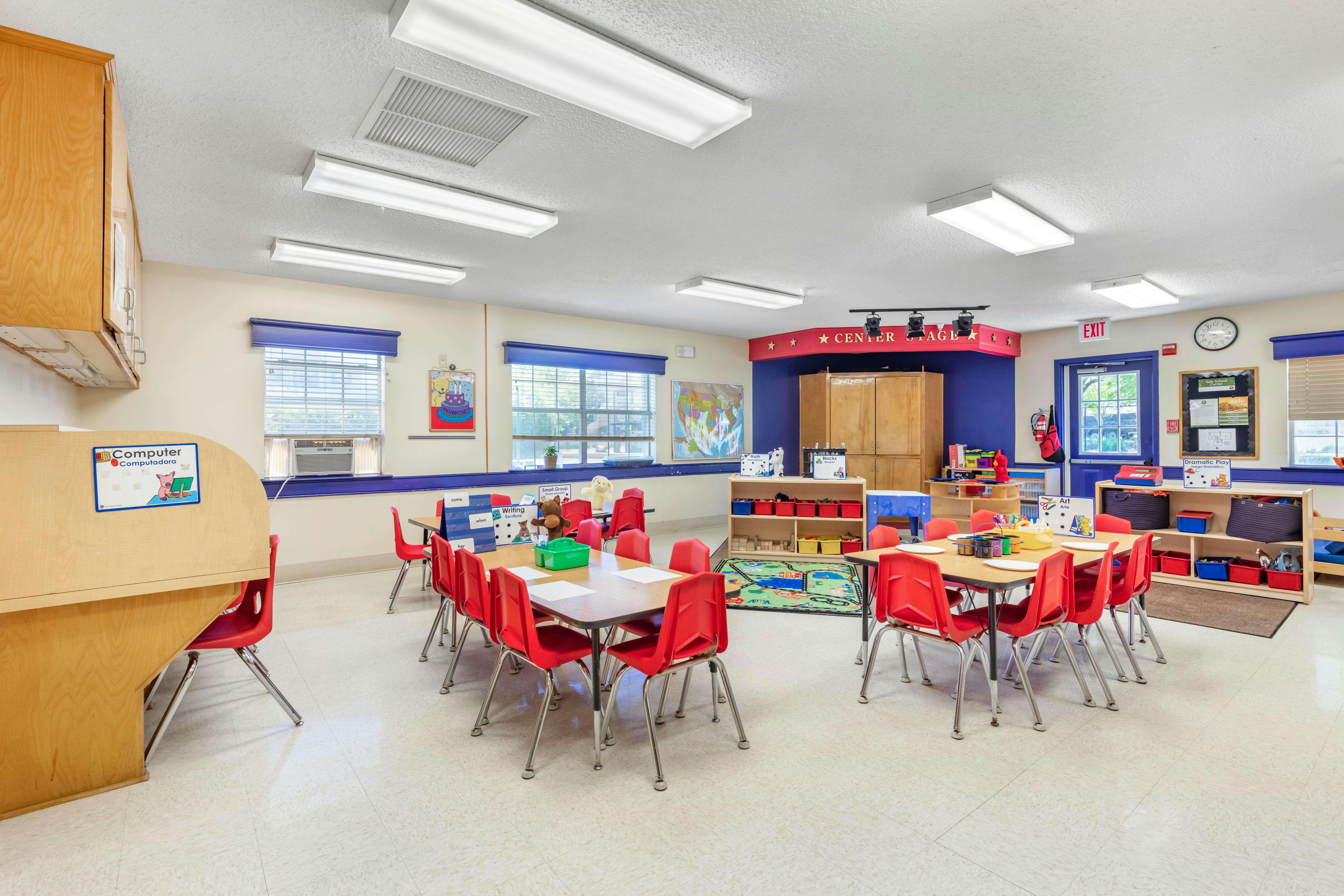 Classroom with small tables and red chairs, computer station, and play areas