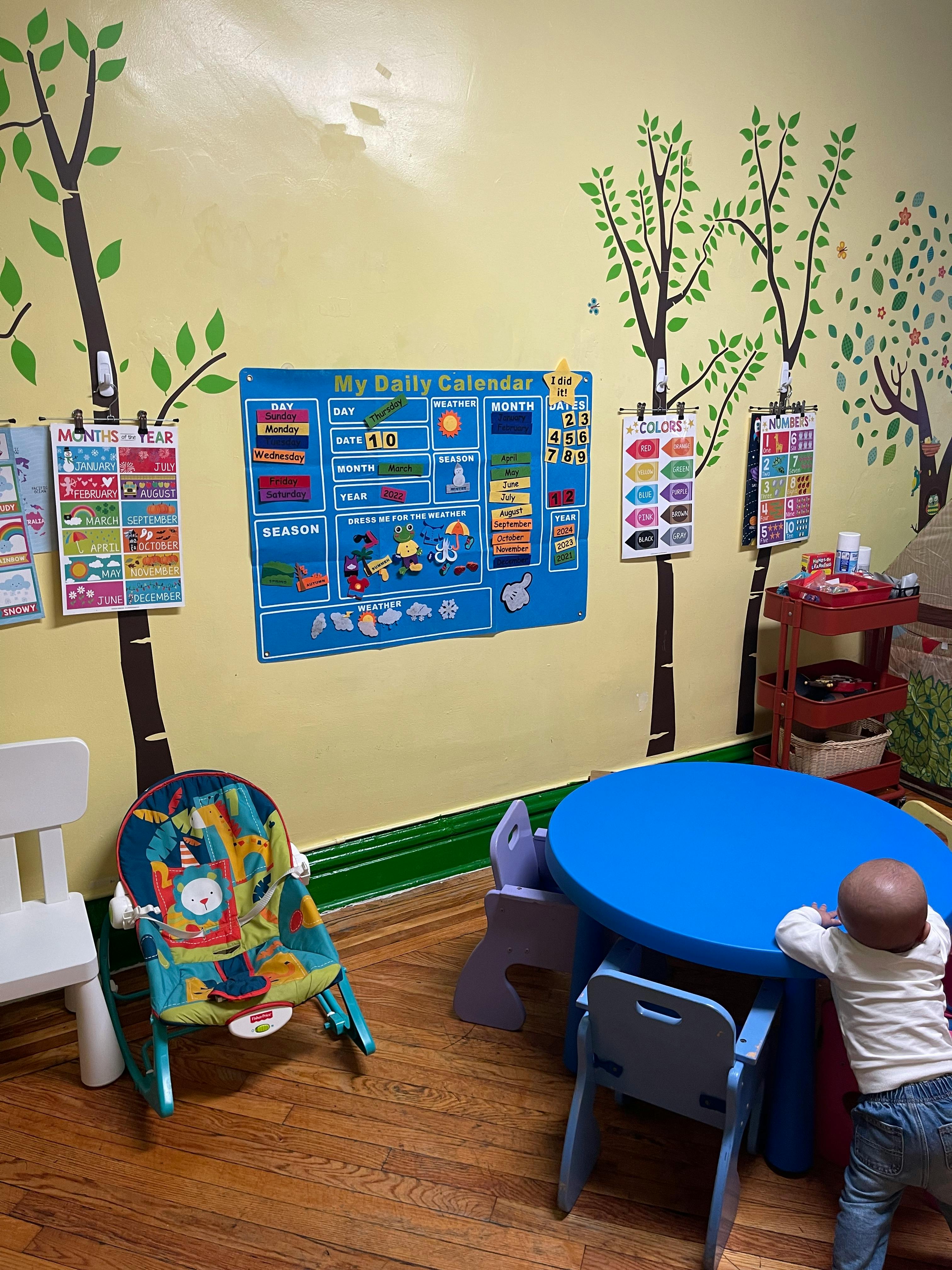 Child standing at a blue table in a room with a daily calendar on the wall