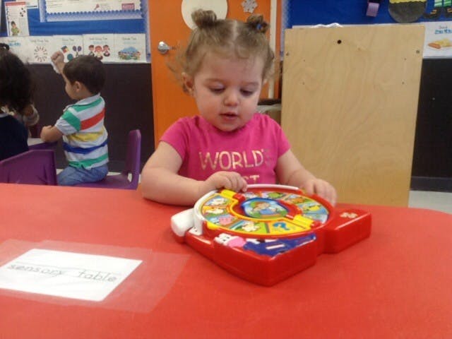 Child playing with a red toy on a red table in a classroom