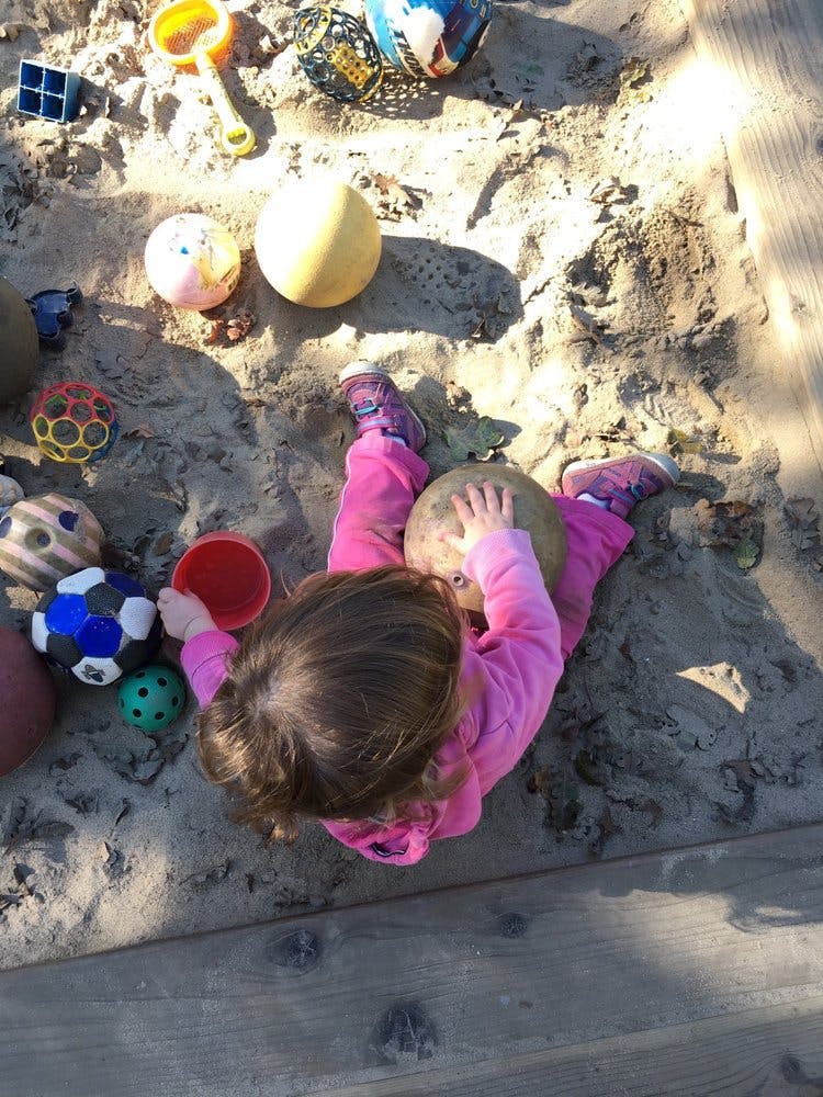 Child playing in a sandbox with balls and toys